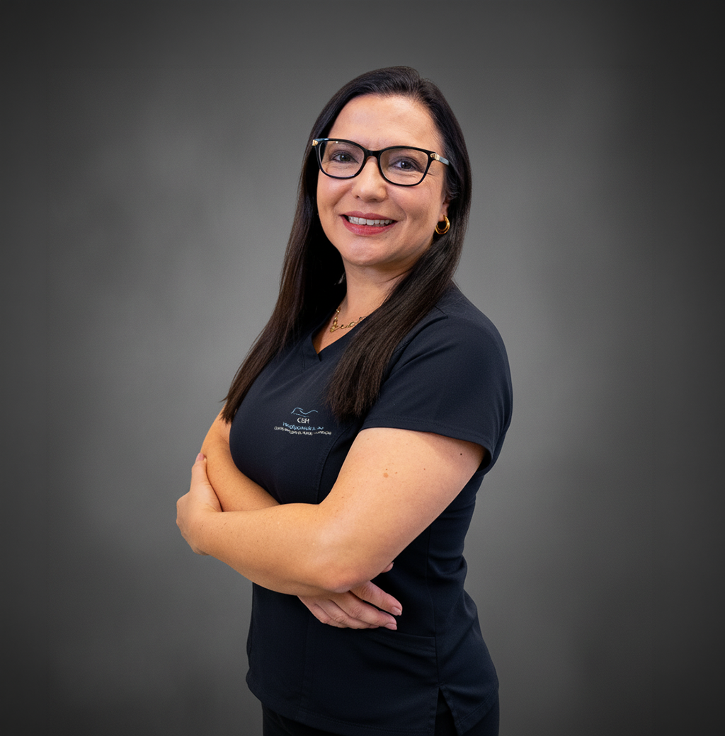 Uma mulher usando óculos e uma camisa preta está de pé com os braços cruzados e sorrindo.