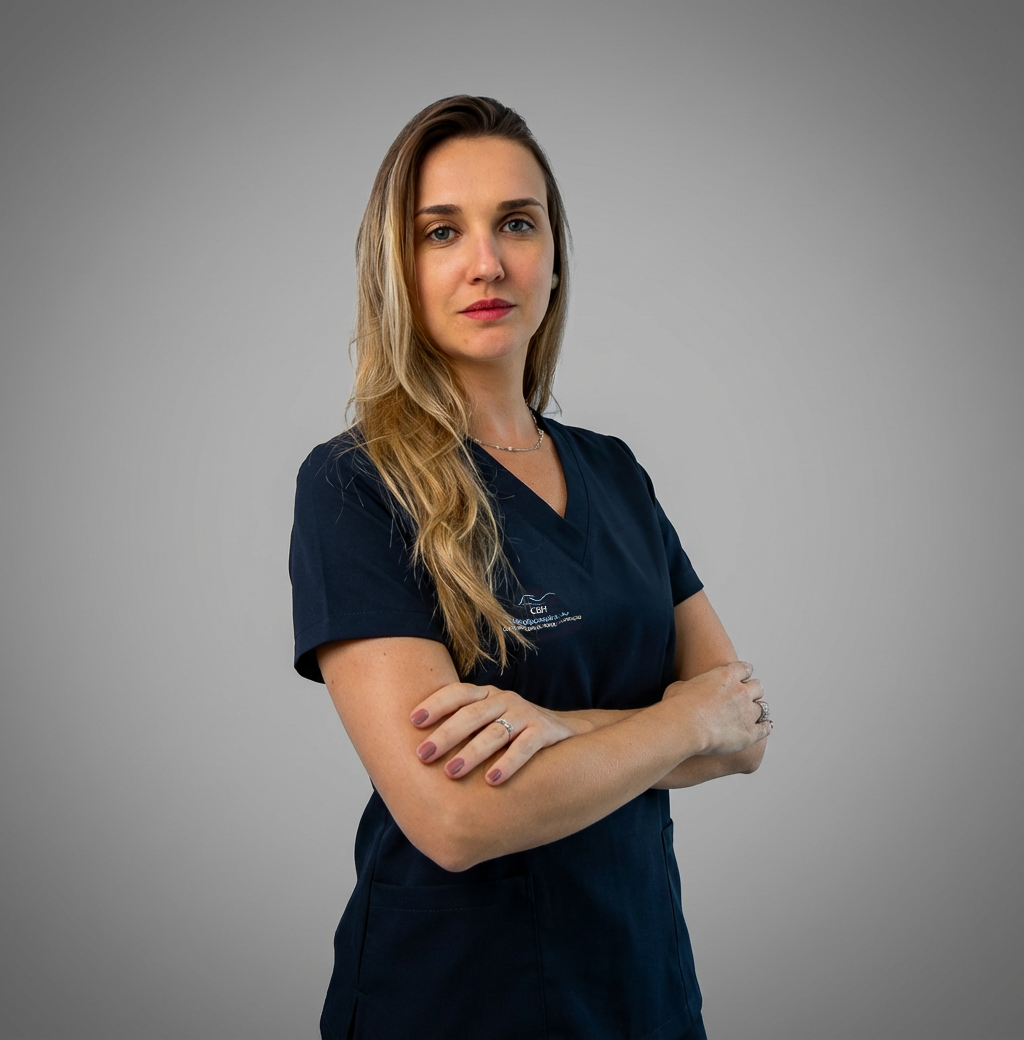 Uma mulher de camisa branca e shorts vermelhos está de pé com os braços cruzados.