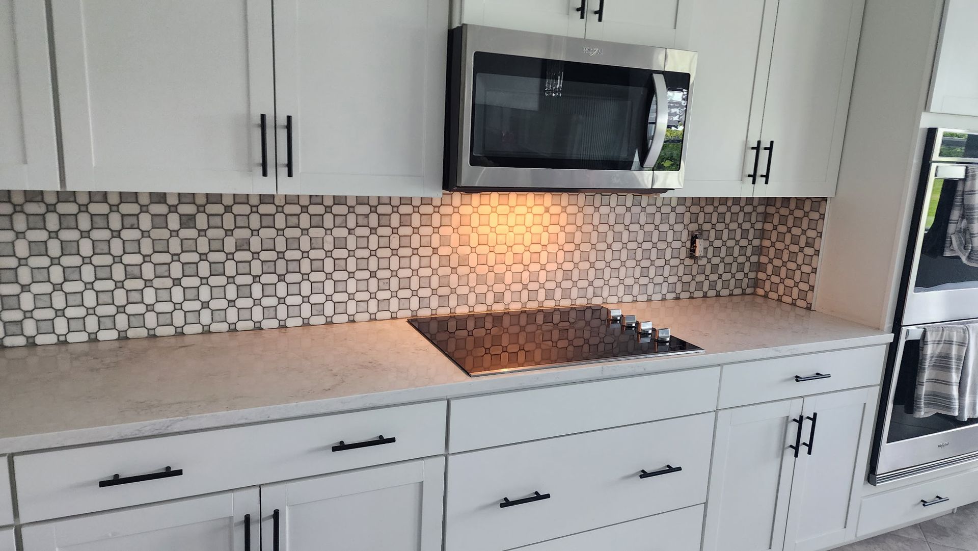 White kitchen with a mosaic tile backsplash, microwave, and cooktop.