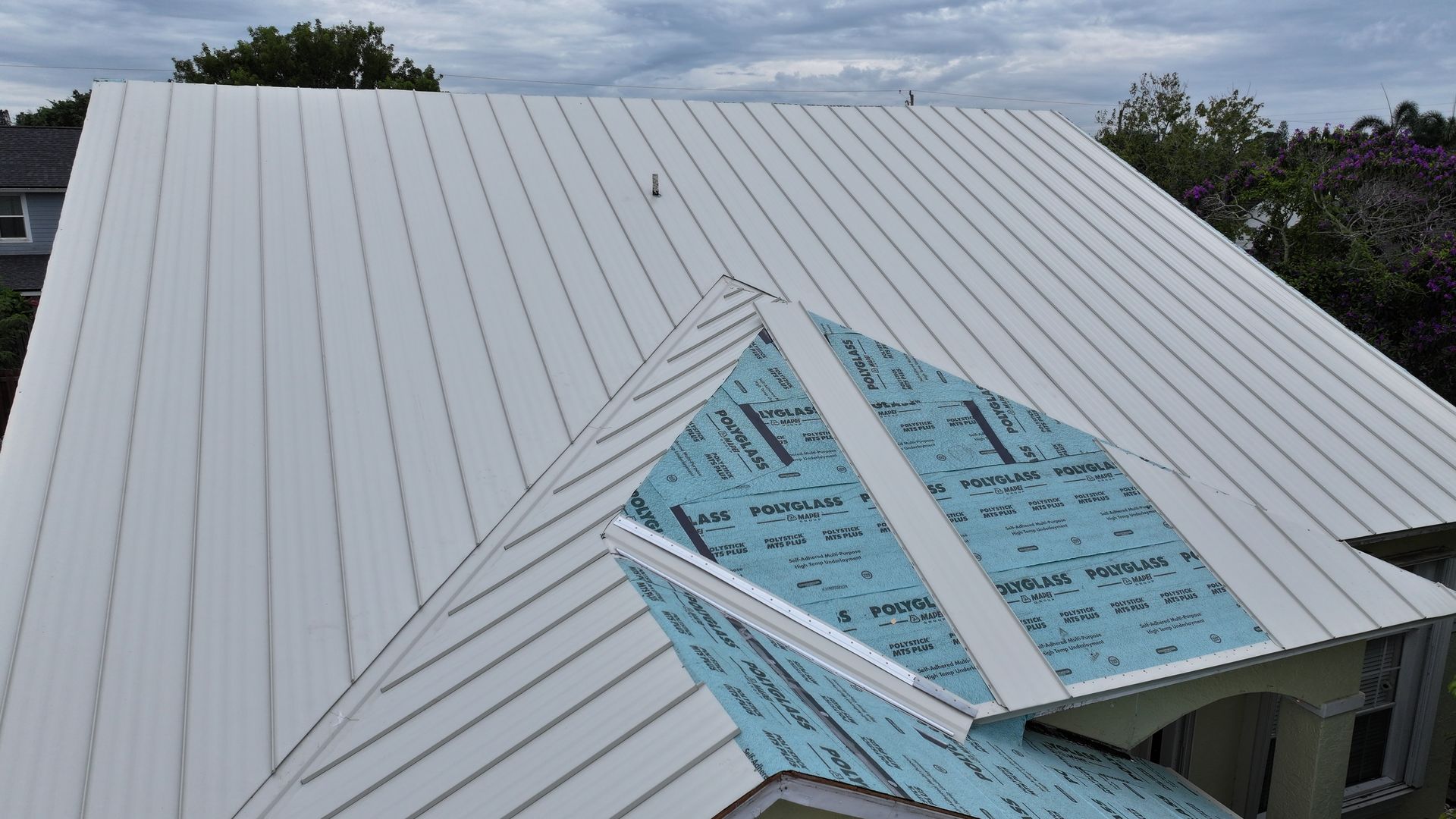 White metal roof being installed on a house with blue underlayment visible on a smaller section.