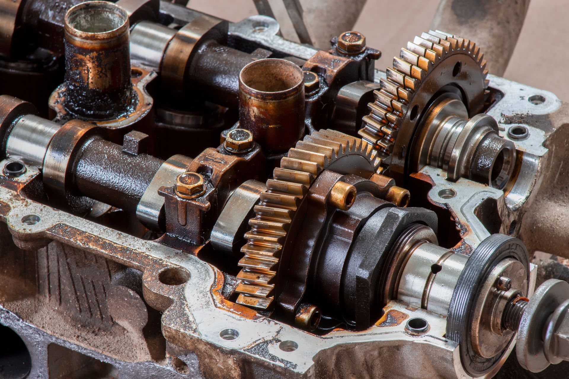 Close-up view of an internal combustion engine cylinder head with visible metal camshafts and timing gears. Close-up view of an internal combustion engine cylinder head with visible metal camshafts and timing gears.