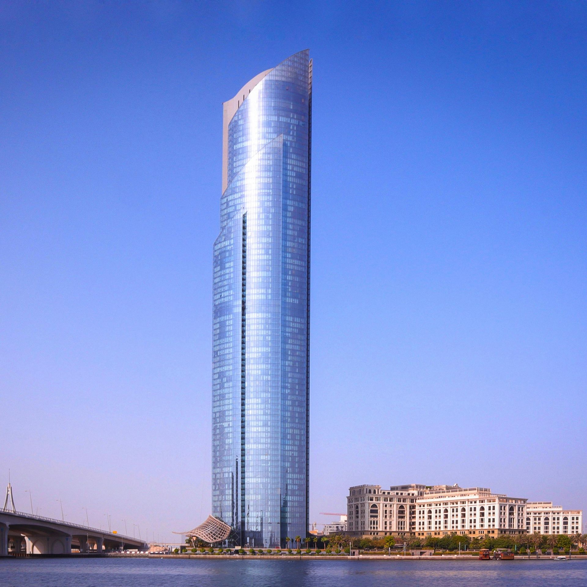 High-rise glass skyscraper against a clear blue sky and waterfront buildings.