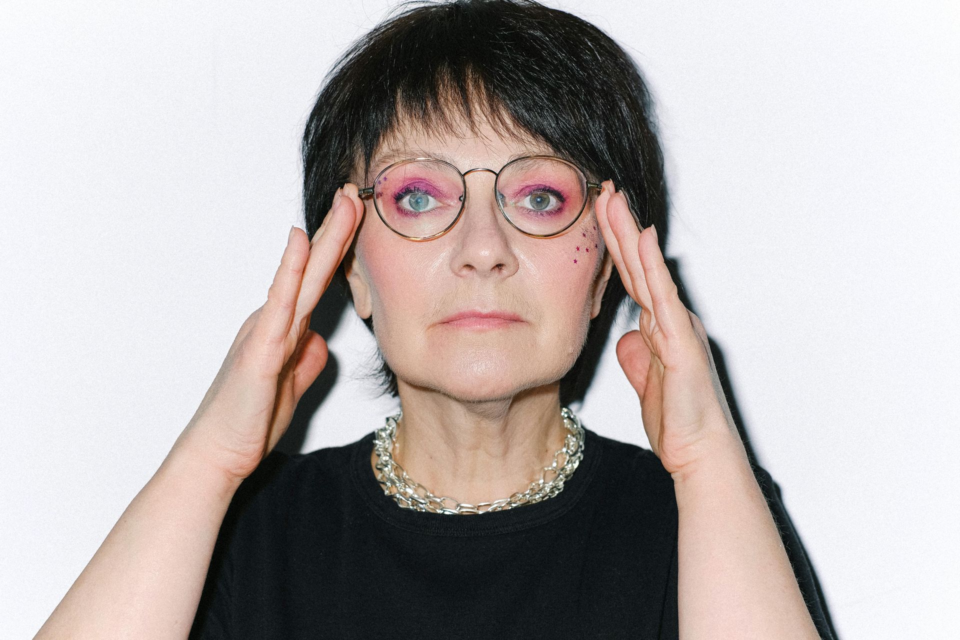 Woman wearing glasses holds hands to temples, looking forward.