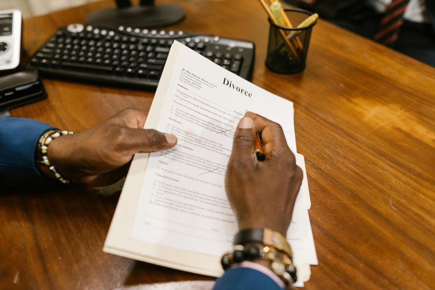 Hands signing a document at a wooden desk with a keyboard and pen holder nearby