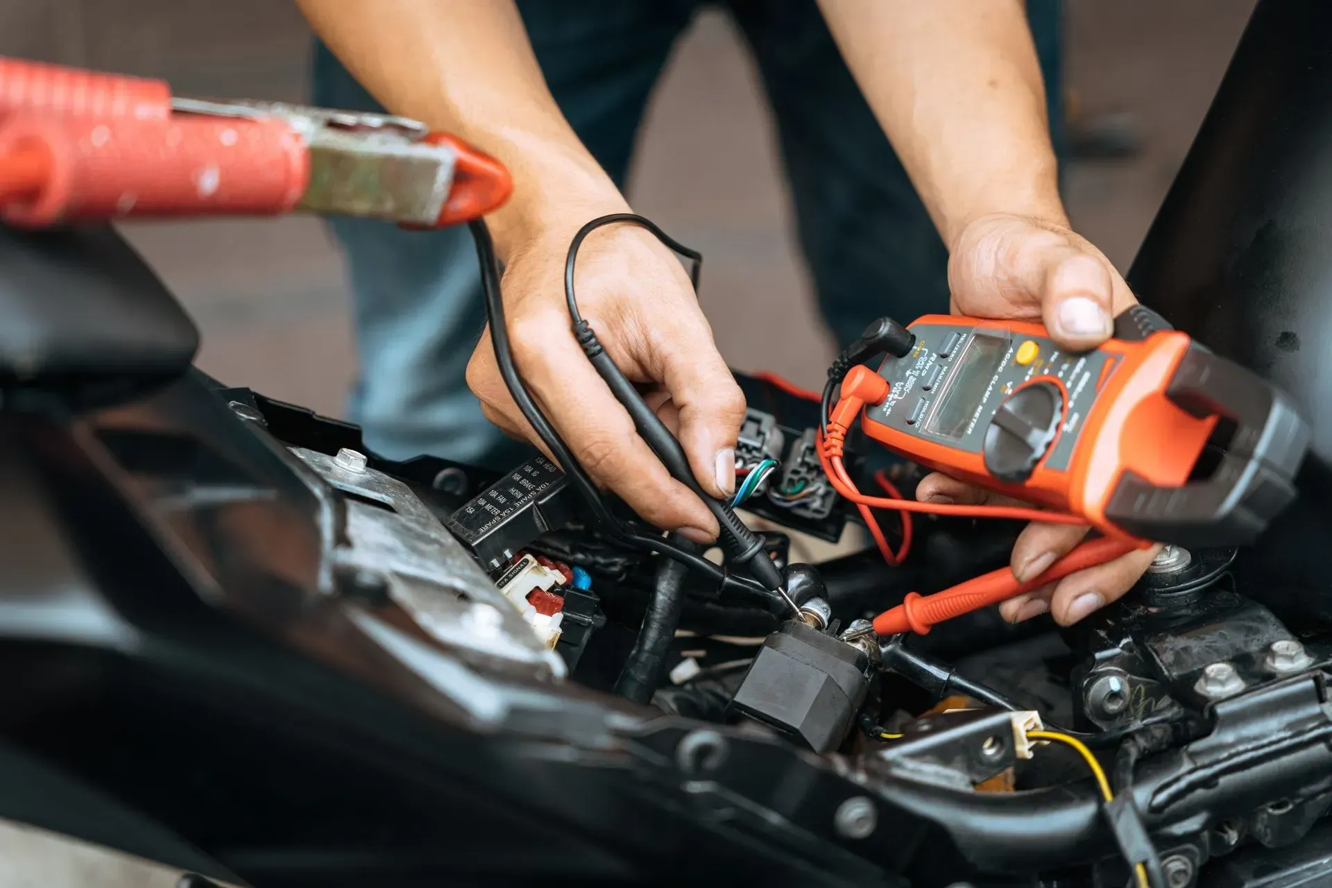 Hands using jumper cables to charge a car battery in an engine bay
