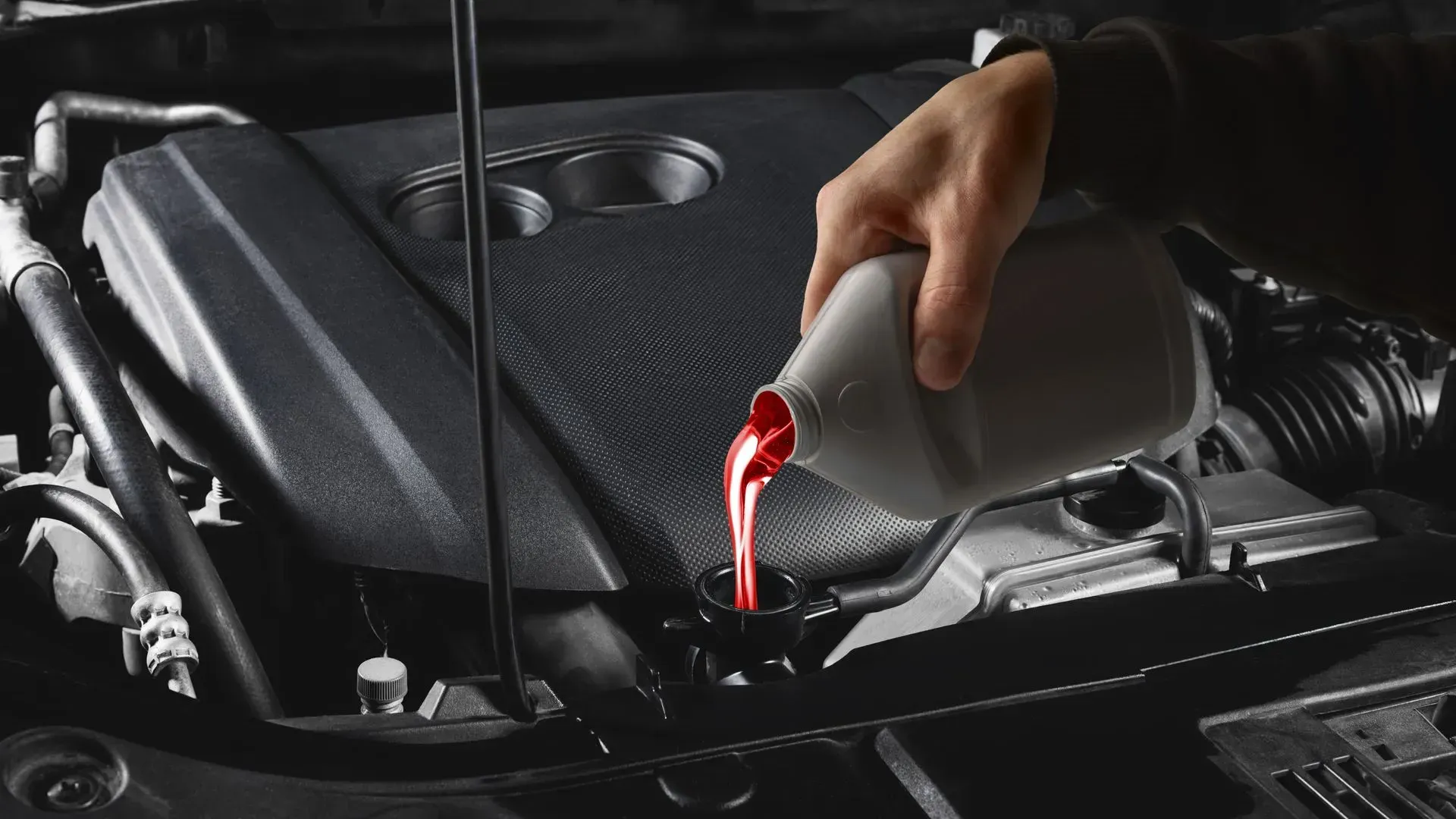 Hand pouring red engine oil into a car engine bay