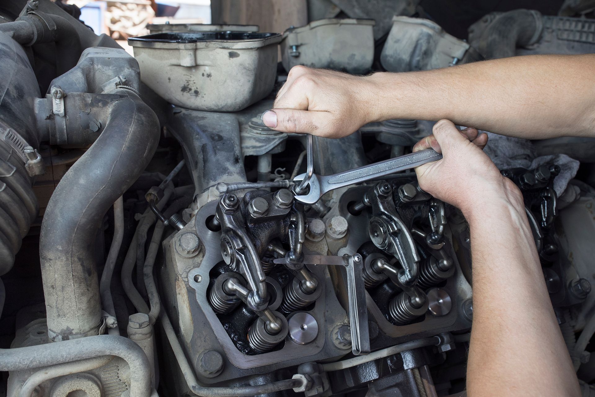 Mechanic adjusting diesel engine valves with a wrench inside a truck engine bay