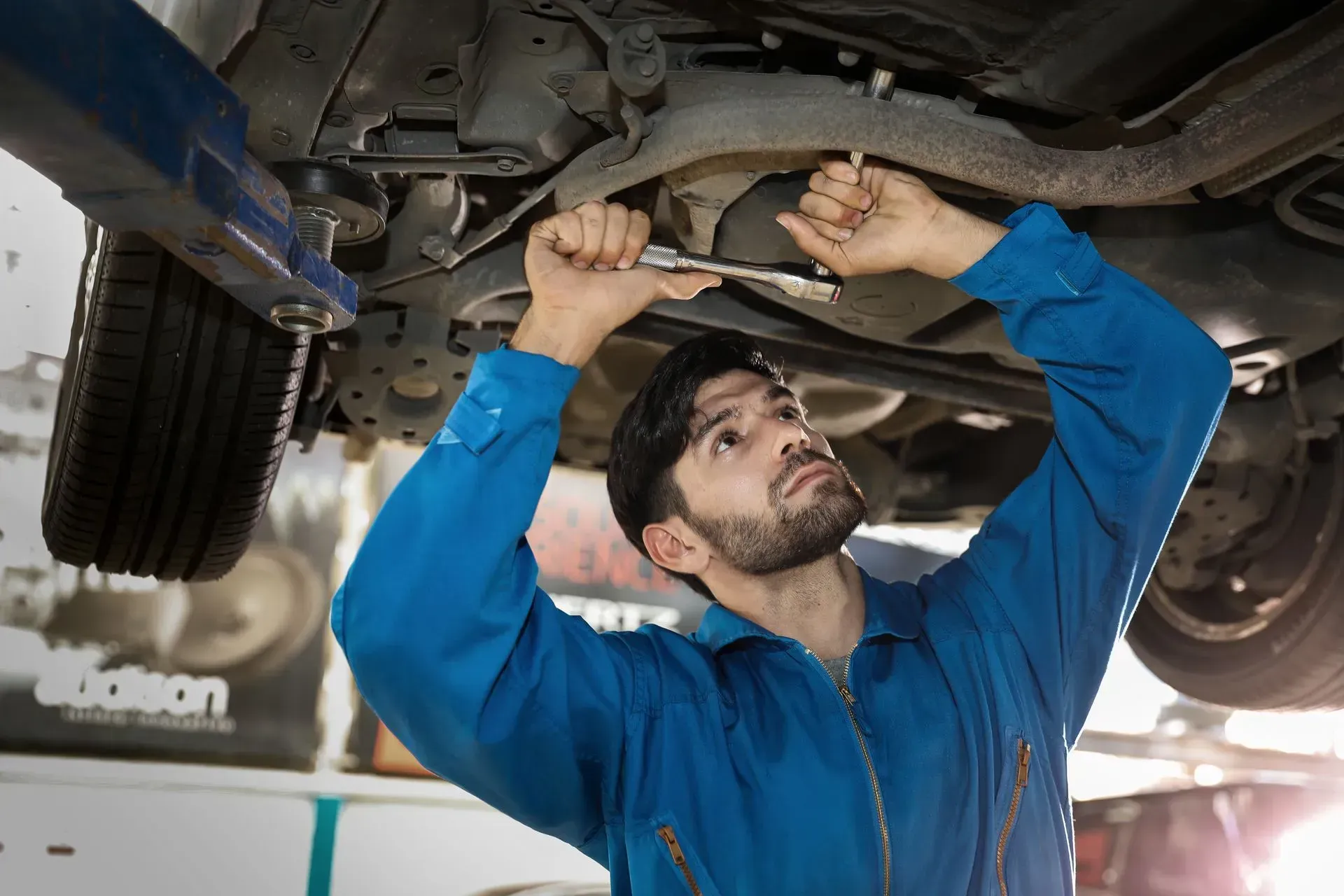 Mechanic in blue coveralls repairs a vehicle underside on a lift in a garage