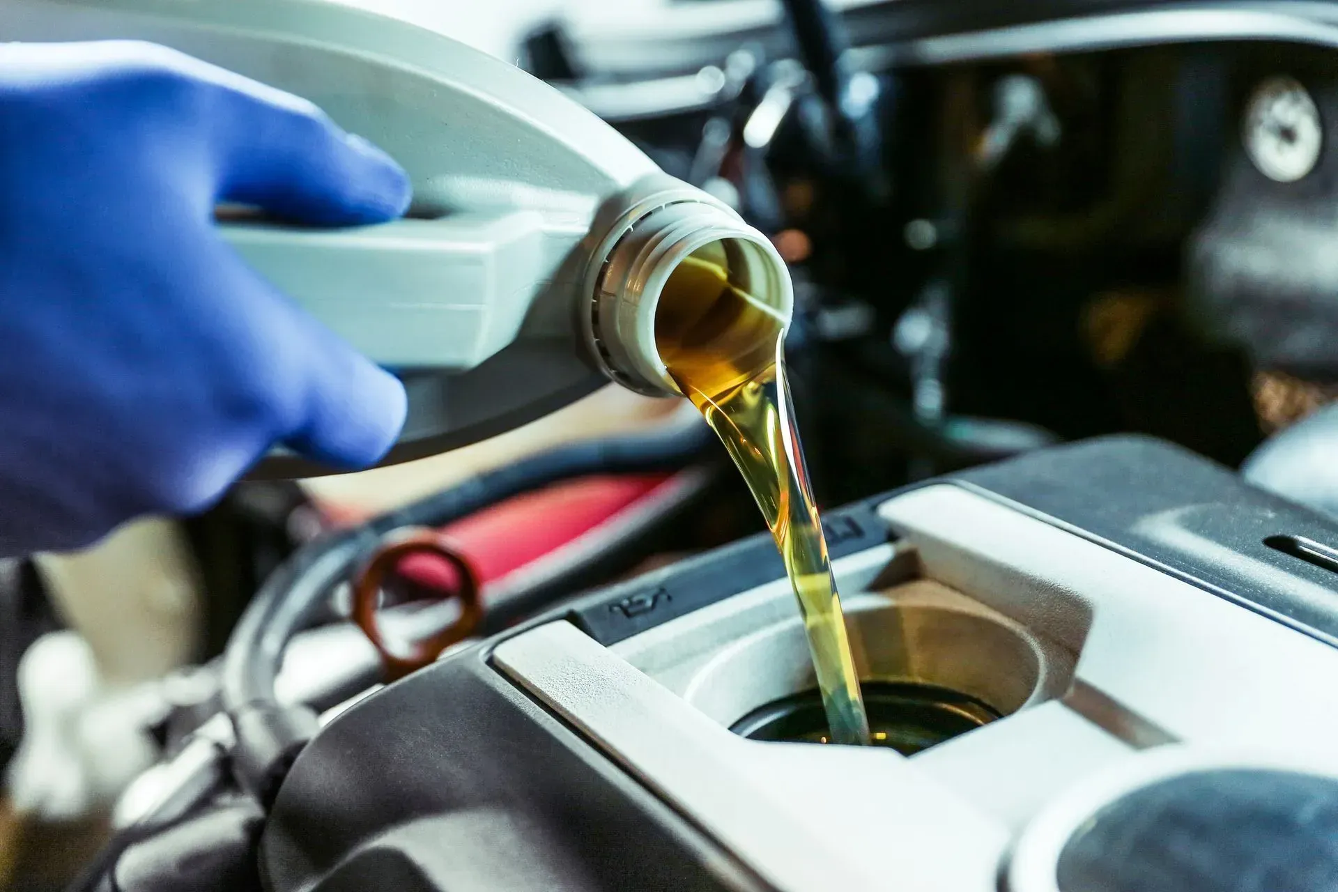 Gloved hand pouring amber motor oil into a car engine reservoir
