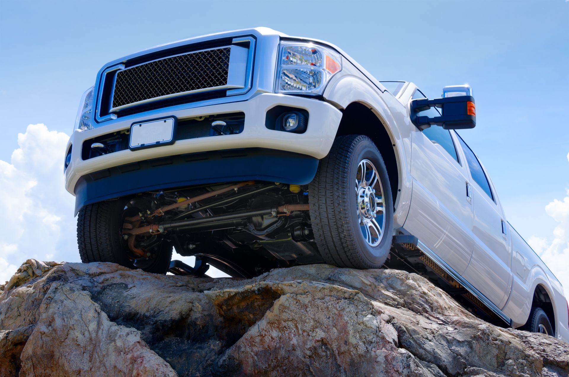 White diesel pickup truck perched on rocks under a blue sky, front view angled upward