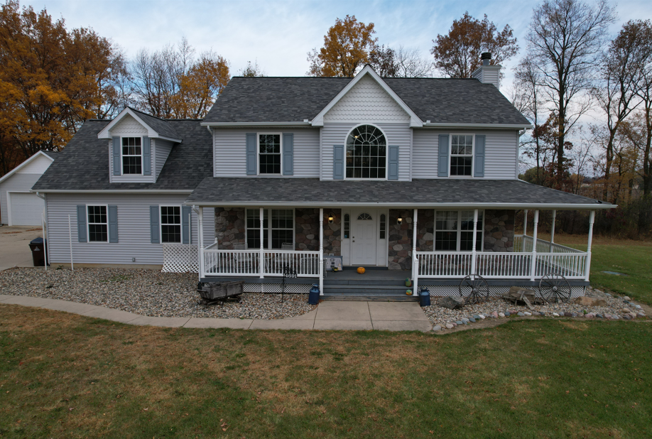 Two-story gray house with porch, shutters, and stone accents, set in a yard with trees.