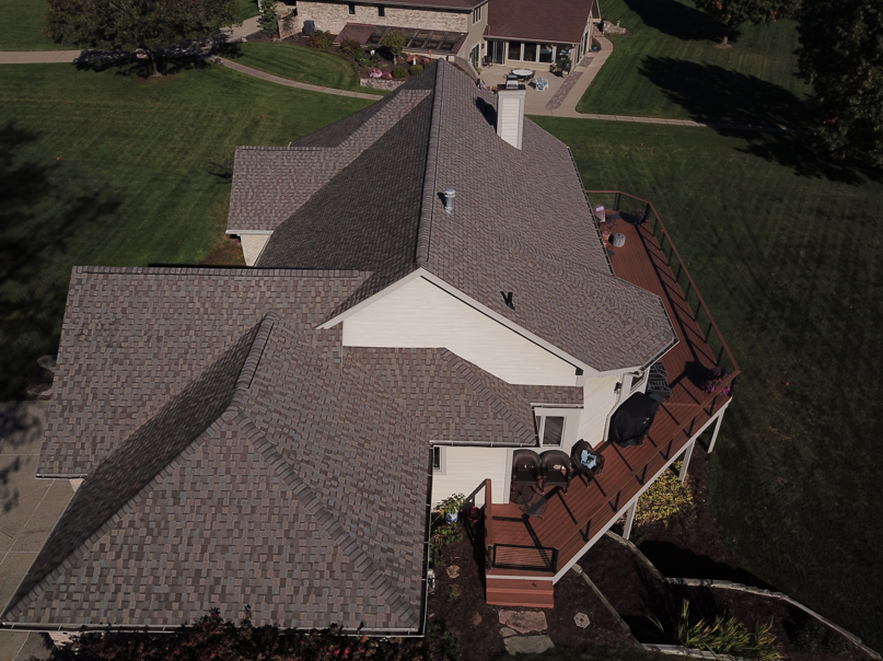 Aerial view of a house with a brown shingled roof, a wooden deck, and a green lawn.