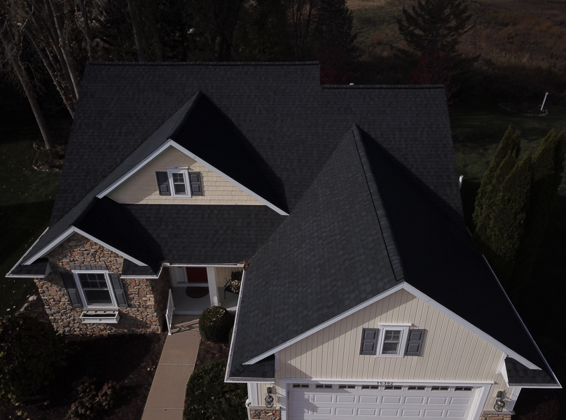 Dark roof on a two-story house with beige siding, brick facade, and a white garage door.