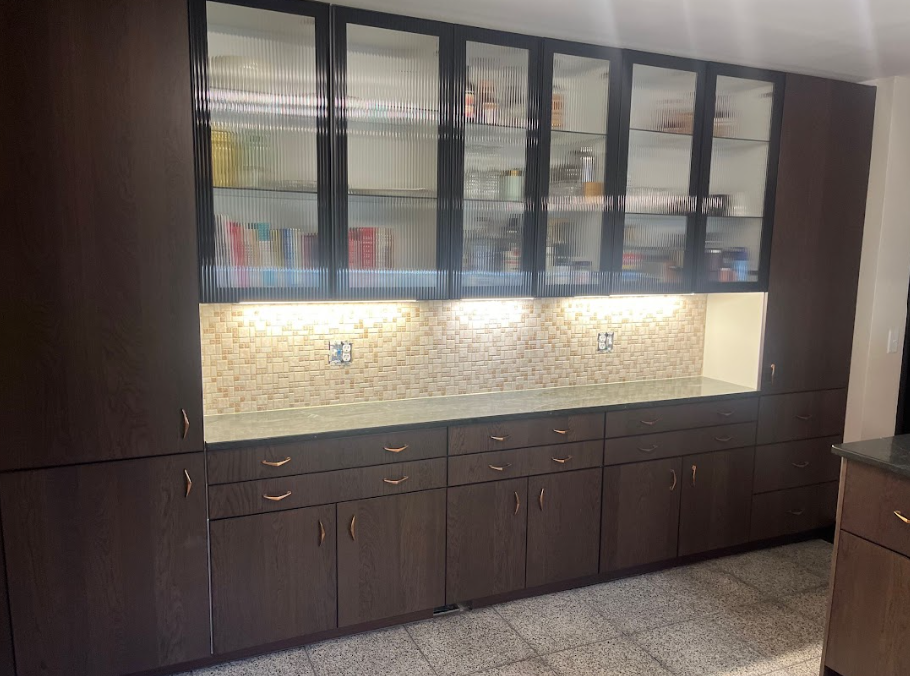 Dark brown kitchen cabinets with glass-front uppers, countertop, and backsplash tiles.