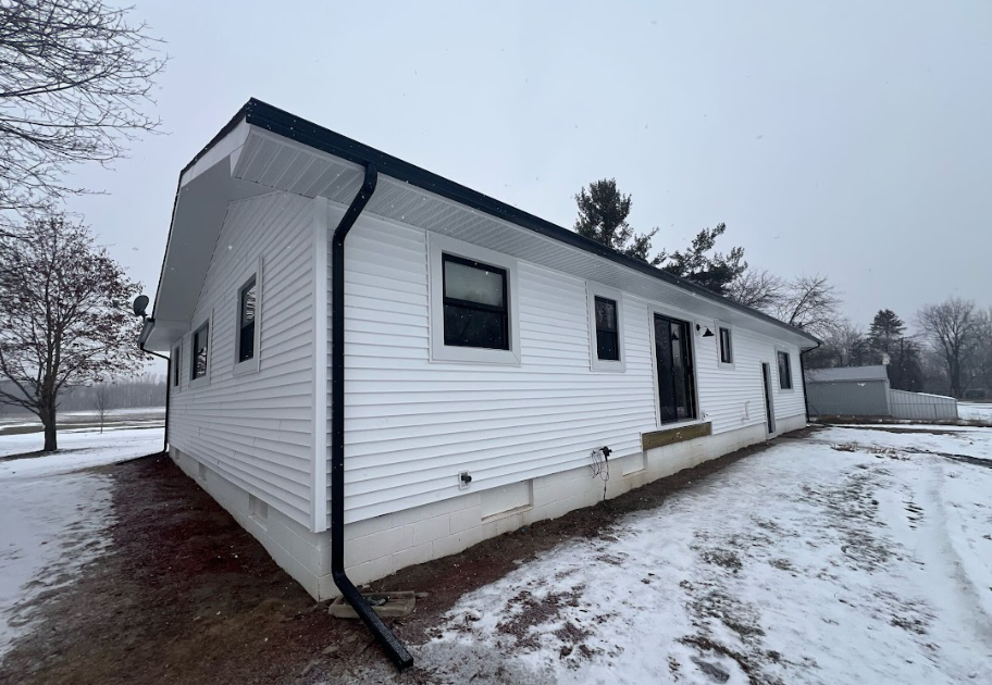 White house with black trim and roof in a snowy landscape.