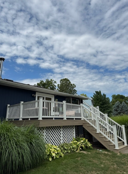 White deck with stairs, lattice skirting, and navy blue house against a cloudy blue sky.