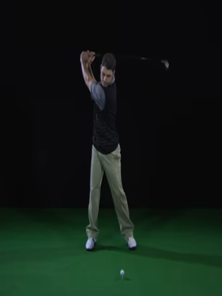 A man is swinging a golf club in front of a large screen.