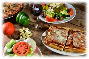 A wooden table topped with plates of food and a glass of wine.