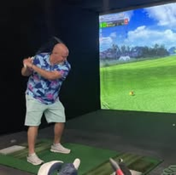 A man is swinging a golf club at a golf ball in a simulator.