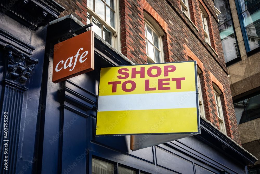 “Shop to let” sign hanging above a café storefront on a brick building “Shop to let” sign hanging above a café storefront on a brick building