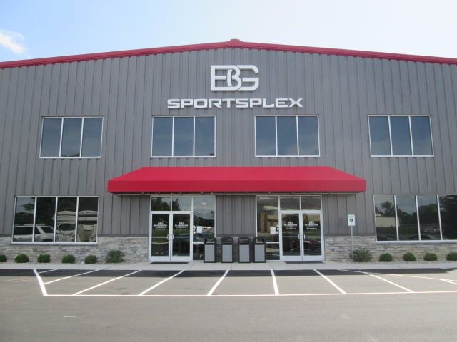 Gray EBG SPORTSPLEX building with red awning over front entrance; windows and parking.