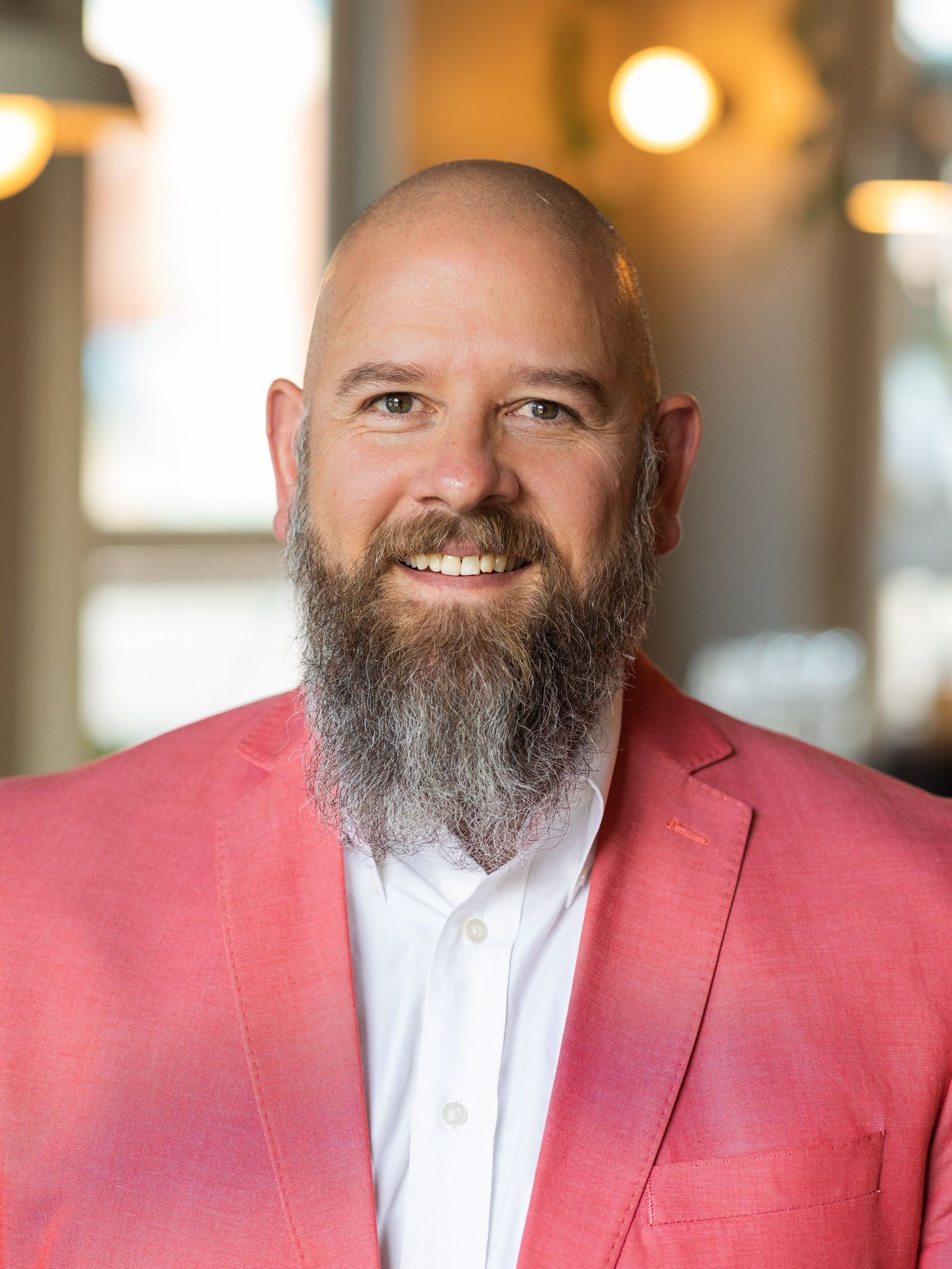 A bald man with a beard is wearing a pink jacket and smiling.