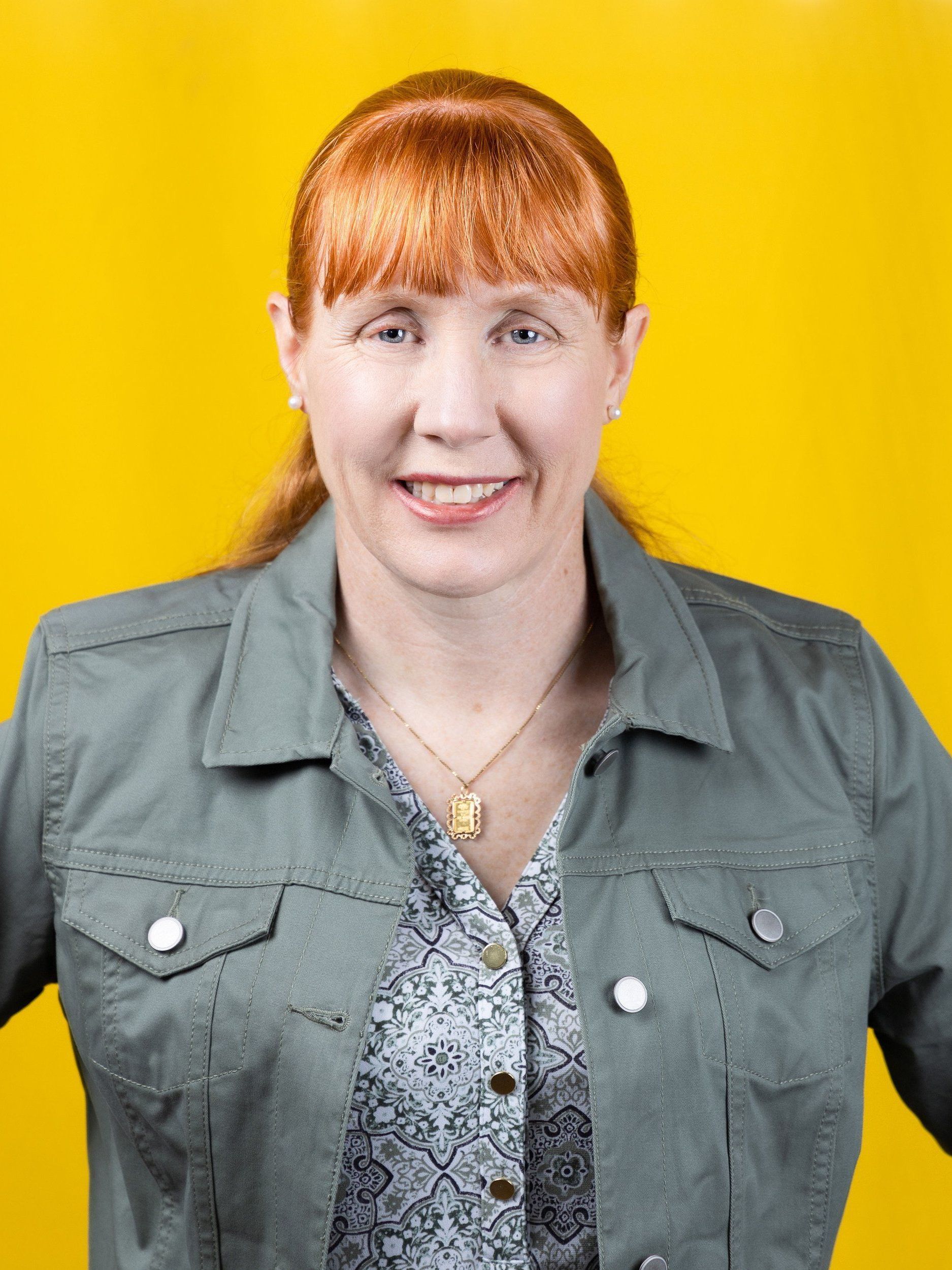 A woman with red hair is wearing a green jacket and a necklace.