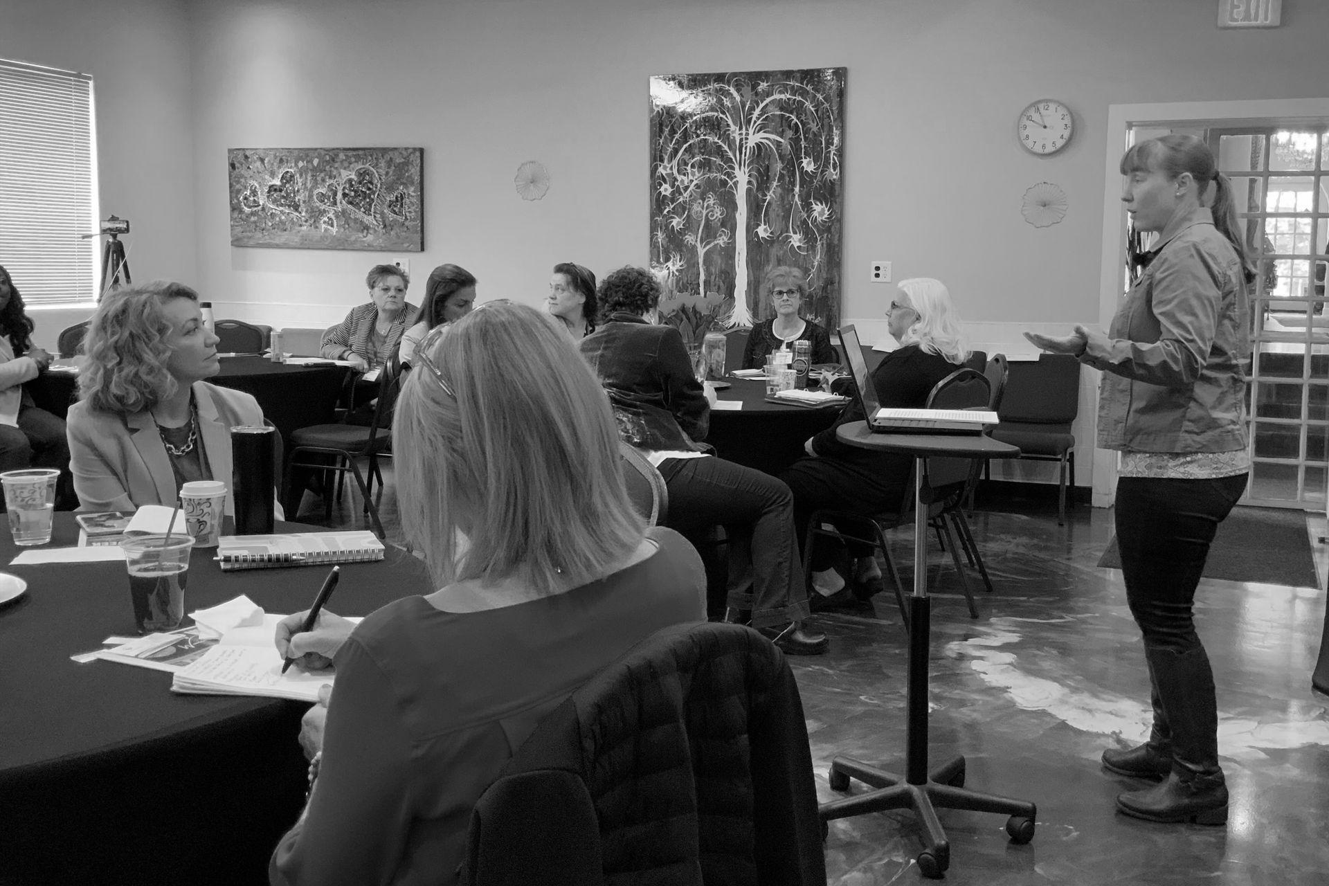 A woman is standing in front of a group of people sitting at tables.