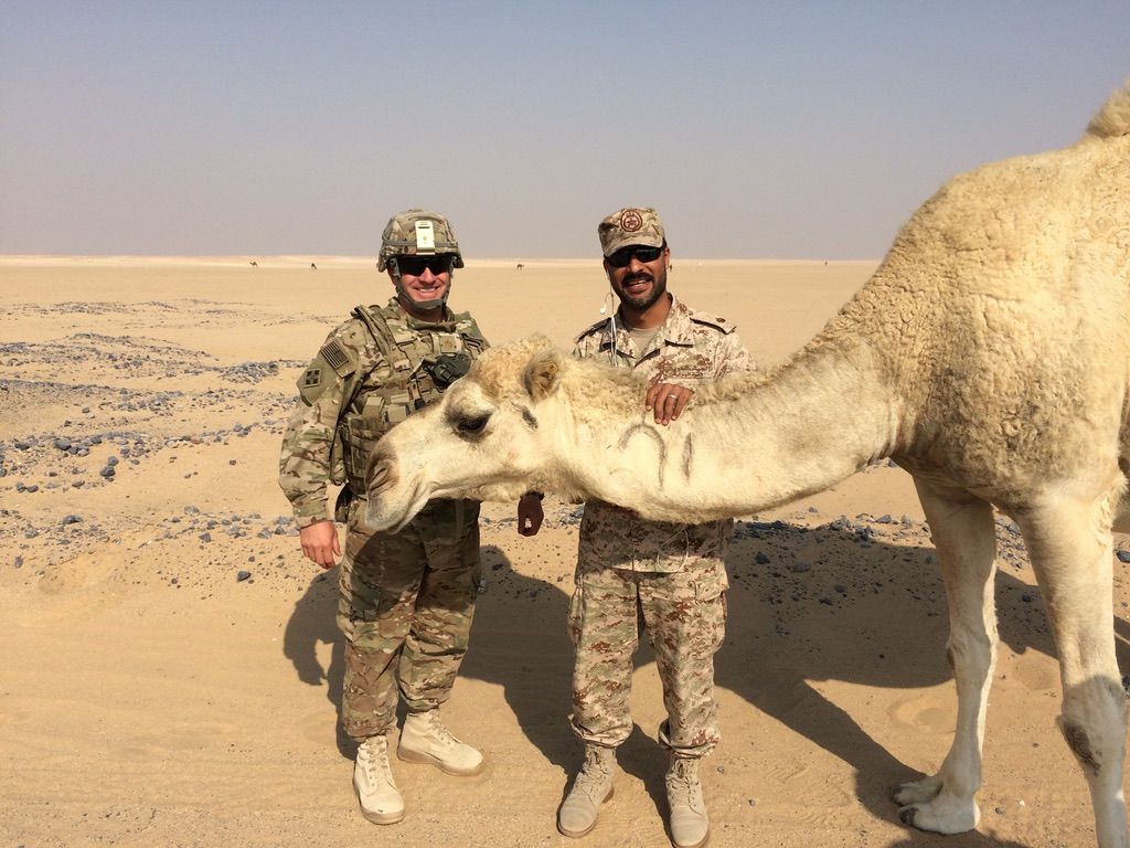 Two soldiers are standing next to a camel in the desert