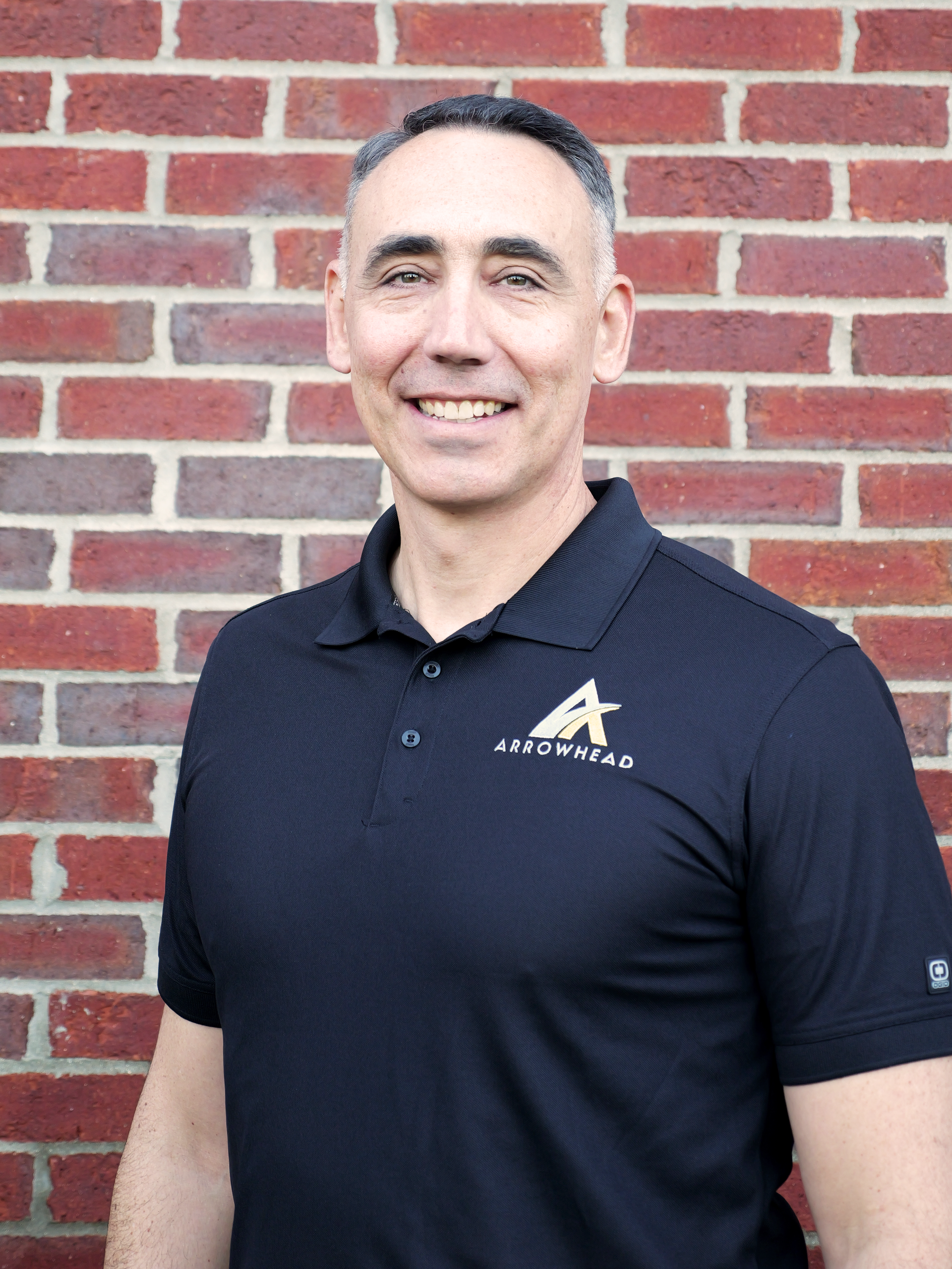 A man in a vest is standing in front of a brick wall.