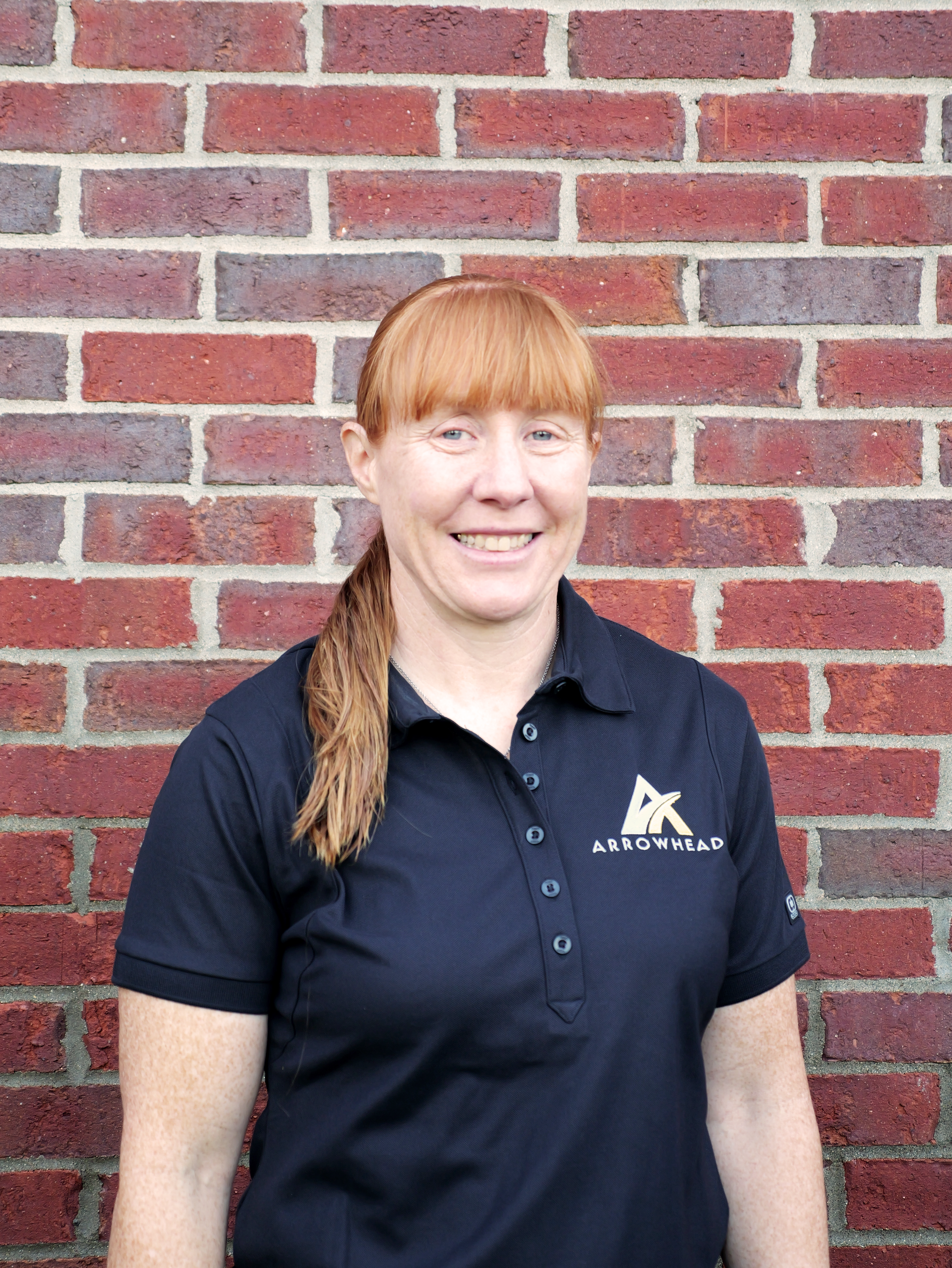 A woman with red hair is standing with her arms crossed and smiling.