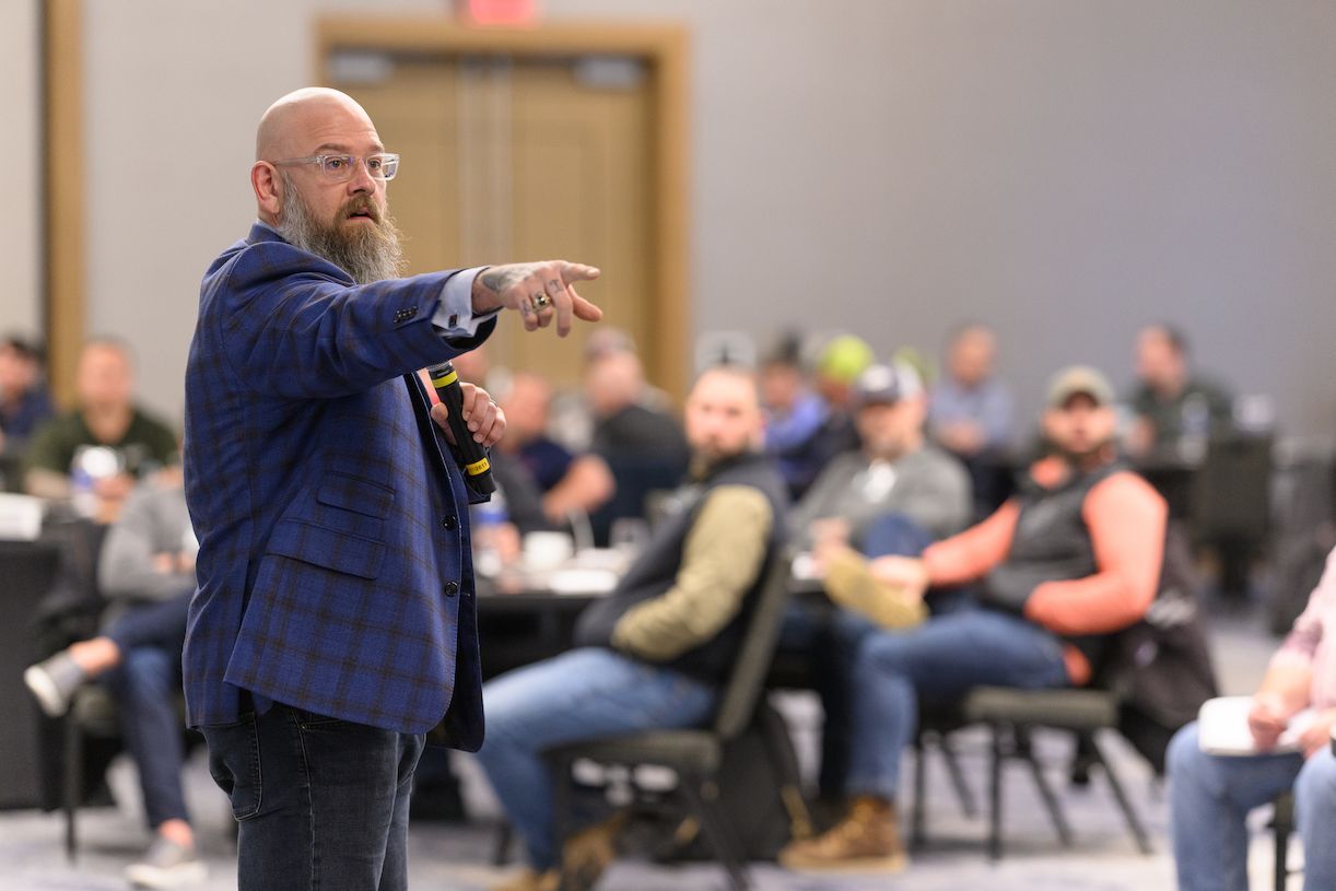 A man with a beard is giving a presentation in front of a group of people.