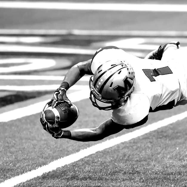 A black and white photo of a football player diving for the ball.