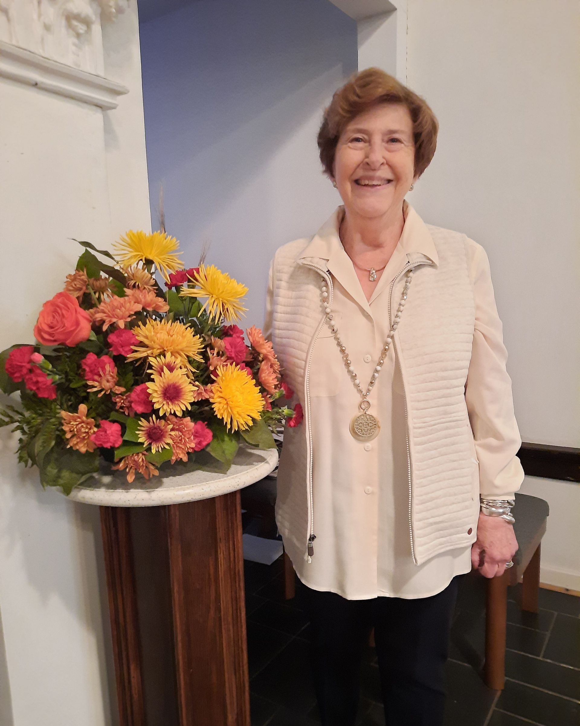 A woman is standing in front of a vase of flowers.