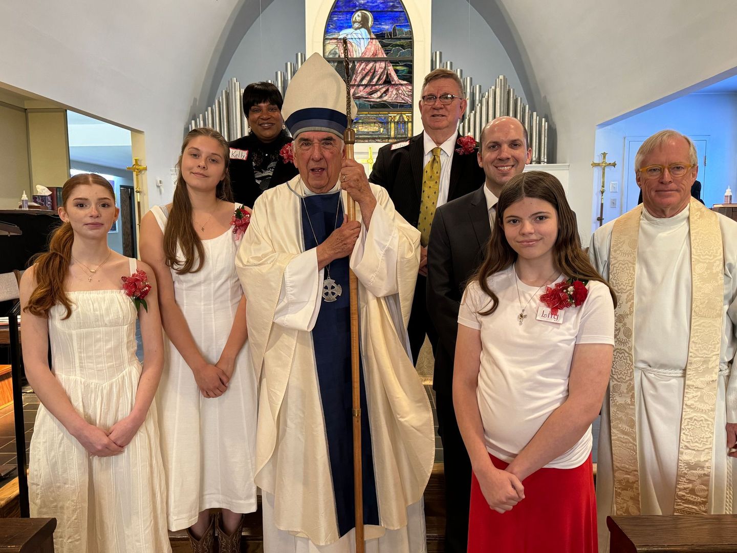 Clergy with attendees in a church, bishop holding staff. People are wearing formal attire.