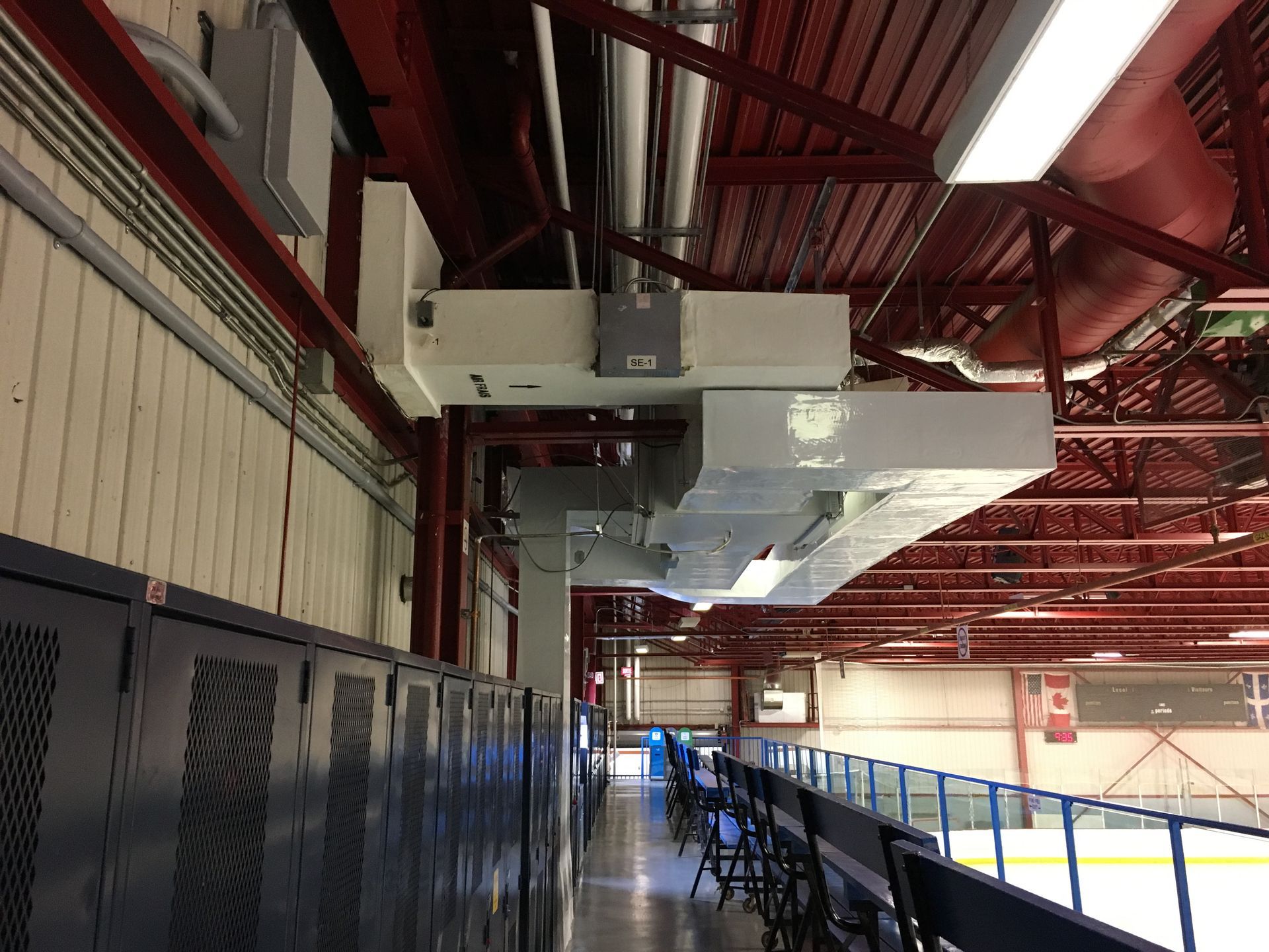 Patinoire intérieure avec casiers, bancs et structures surélevées. Teintes rouges et bleues, avec composants électriques suspendus.