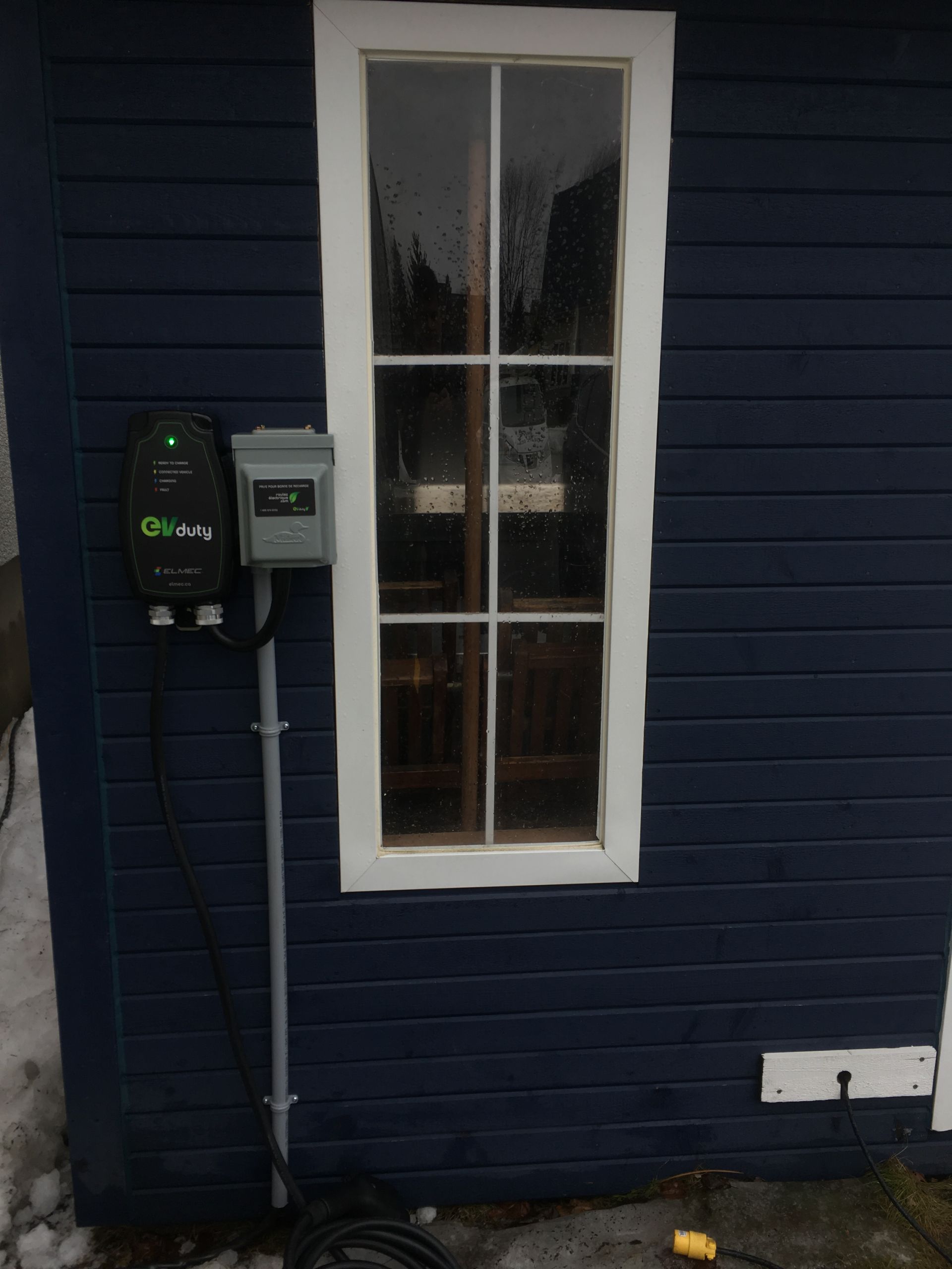 Bâtiment bleu avec une fenêtre et une borne de recharge pour véhicule électrique.