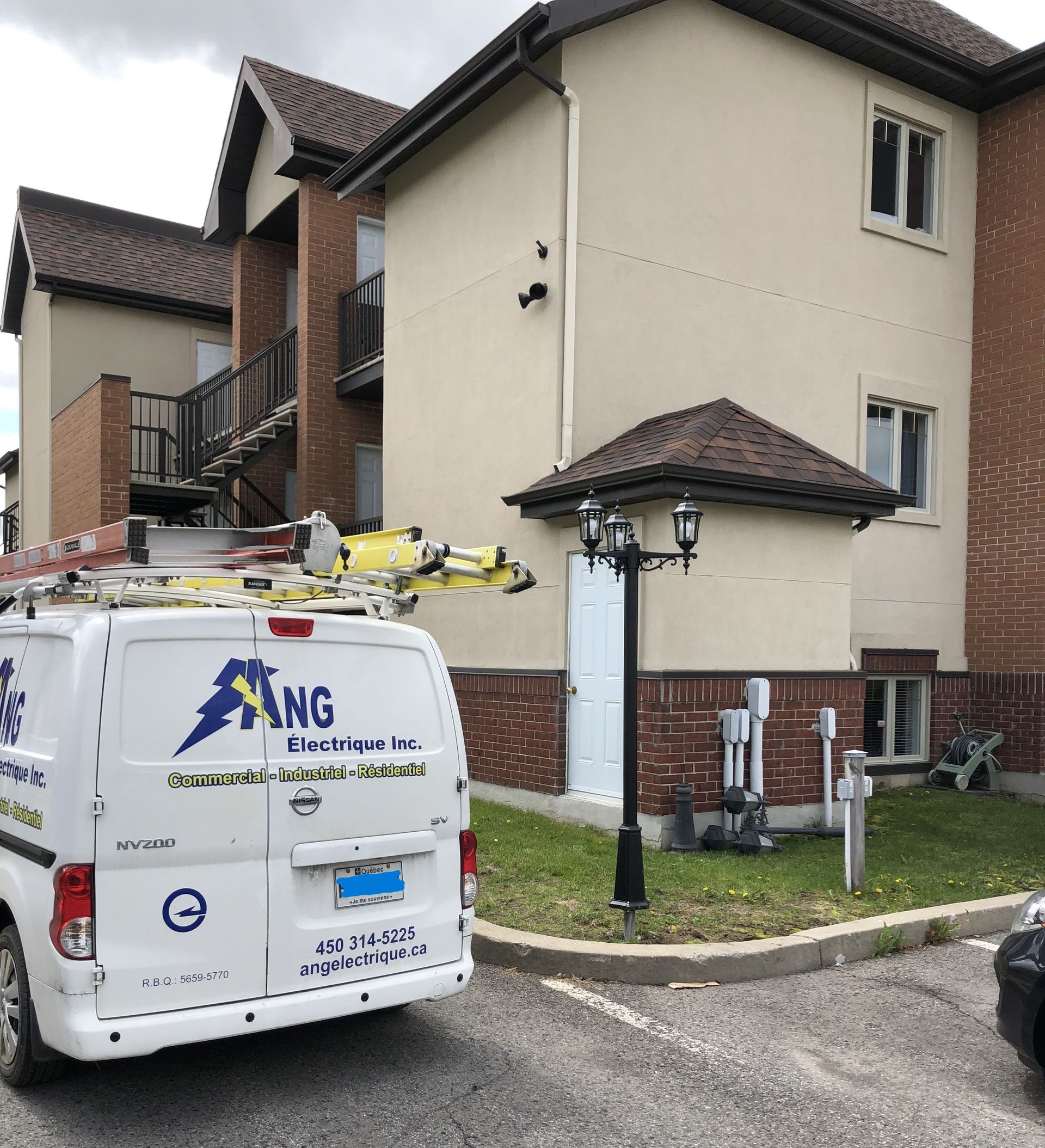 Fourgon électrique ANG stationné à côté d'un immeuble à plusieurs unités, probablement en train d'entretenir les composants électriques extérieurs.