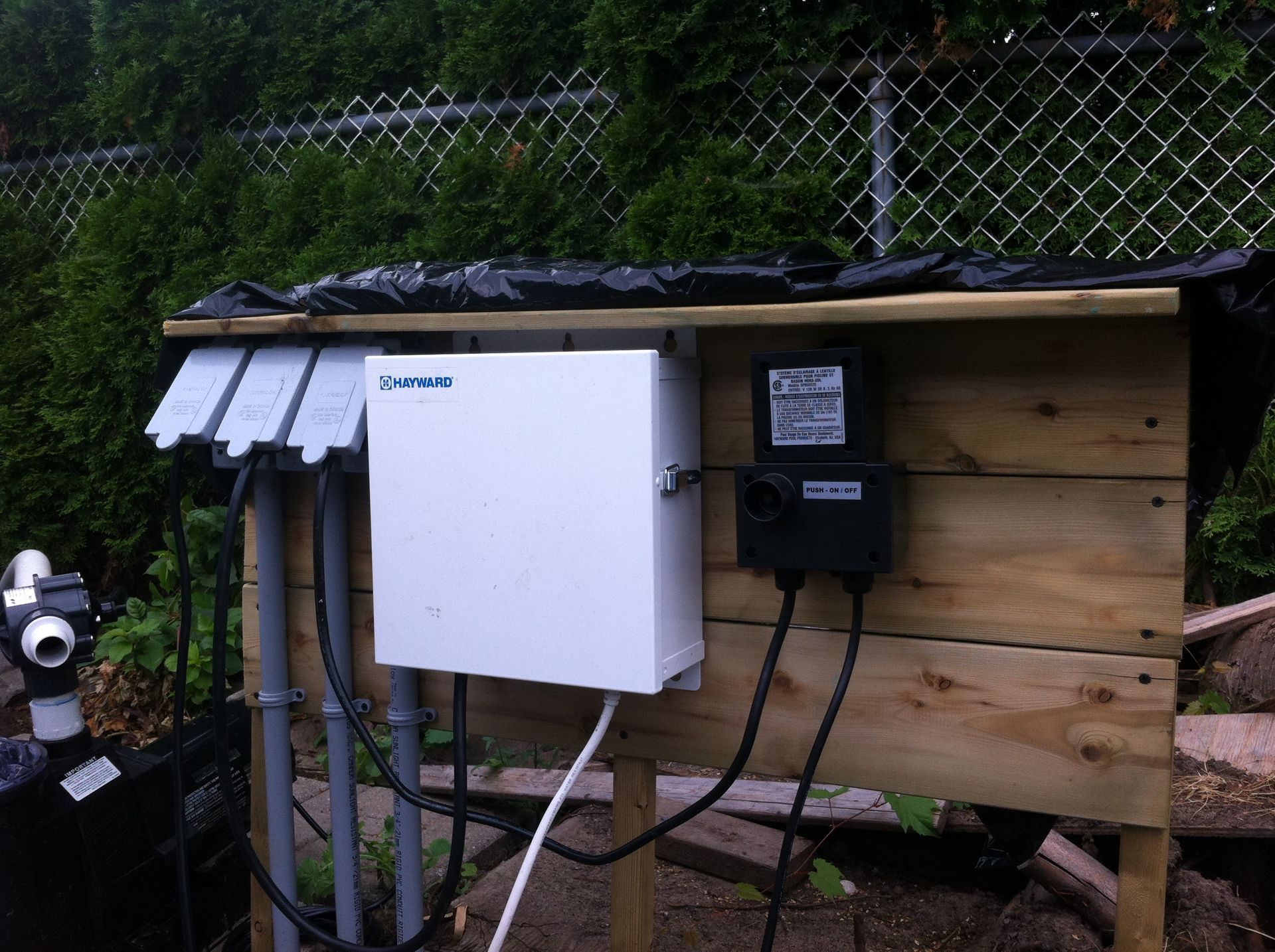 Coffret en bois avec composants électriques à l'extérieur, comprenant un coffret blanc étiqueté « Pentair » et un coffret de commande noir.