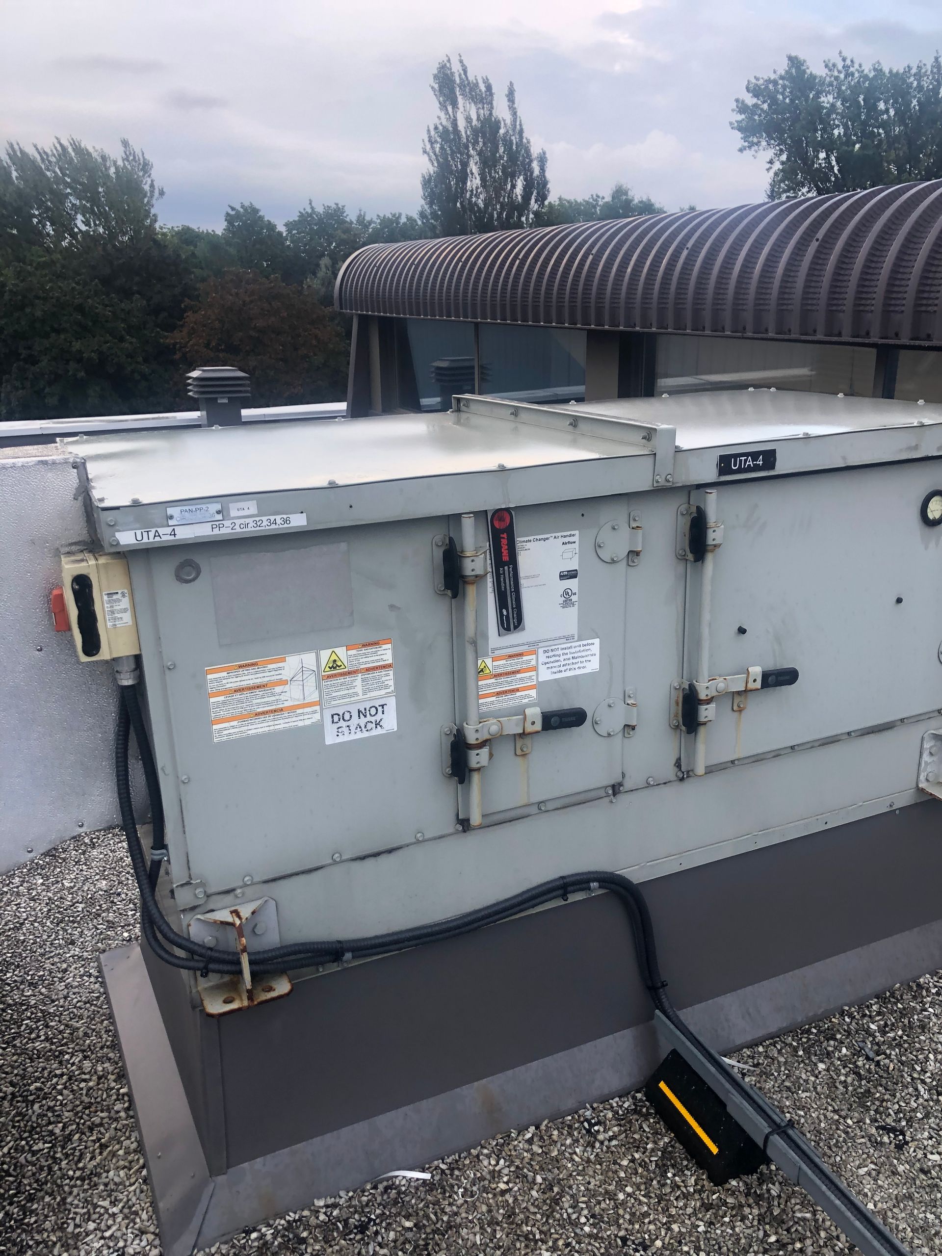 Unité CVC grise sur un toit plat avec un ciel nuageux et des arbres en arrière-plan.