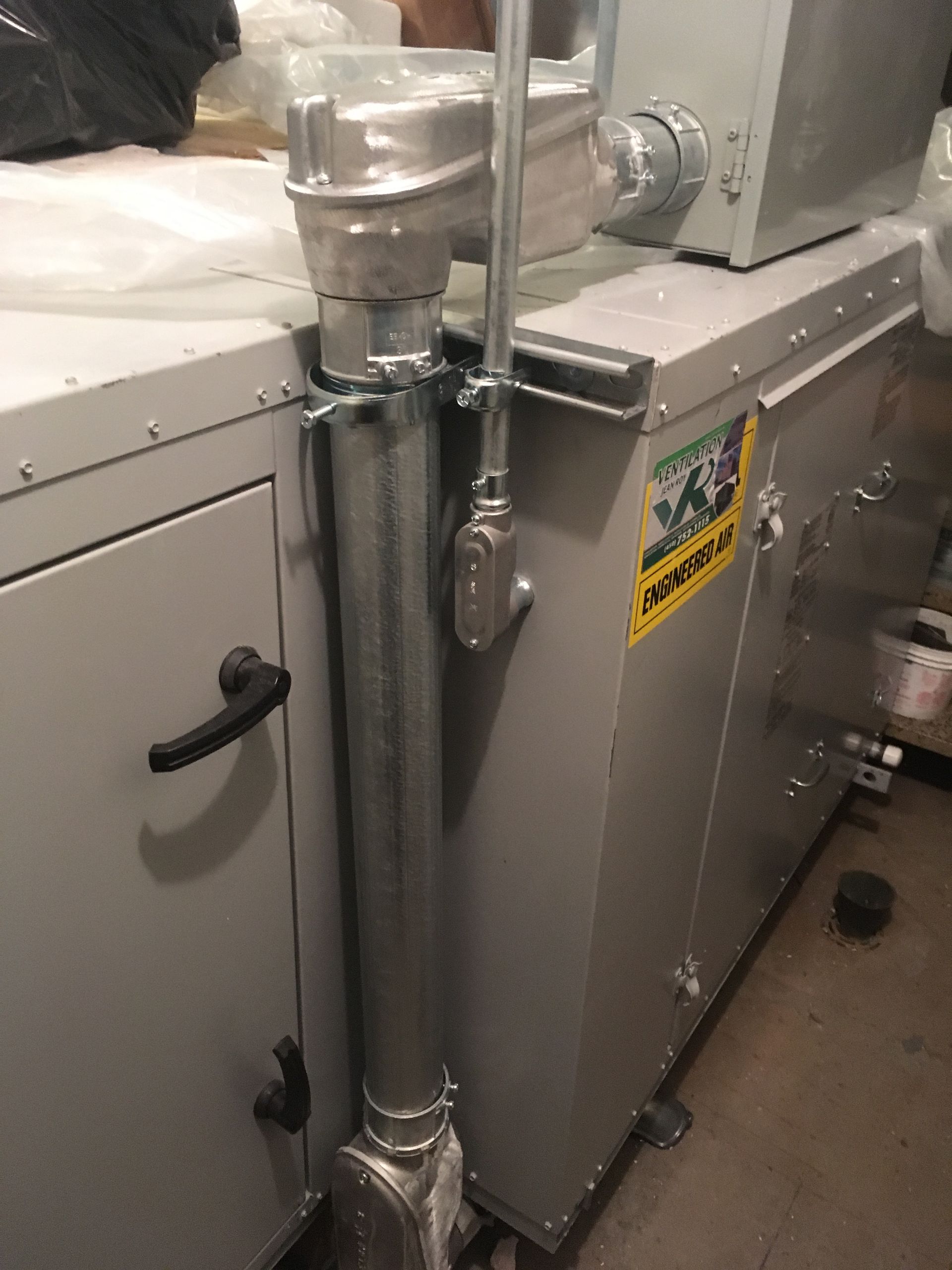 Une machine industrielle en métal avec conduit électrique, grise avec poignée noire et autocollant jaune.