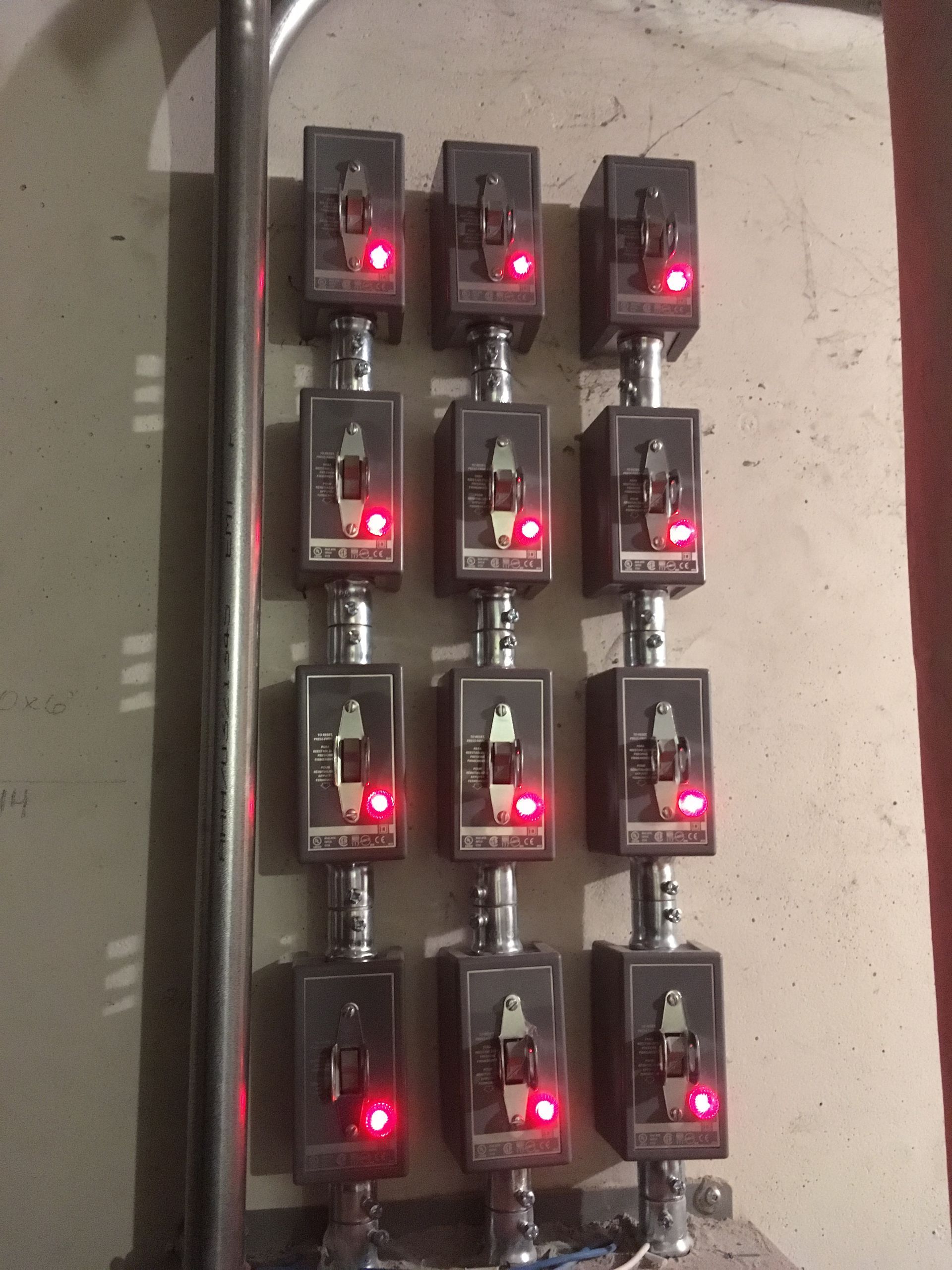 Un panneau de douze interrupteurs noirs avec voyants rouges, monté sur un mur.