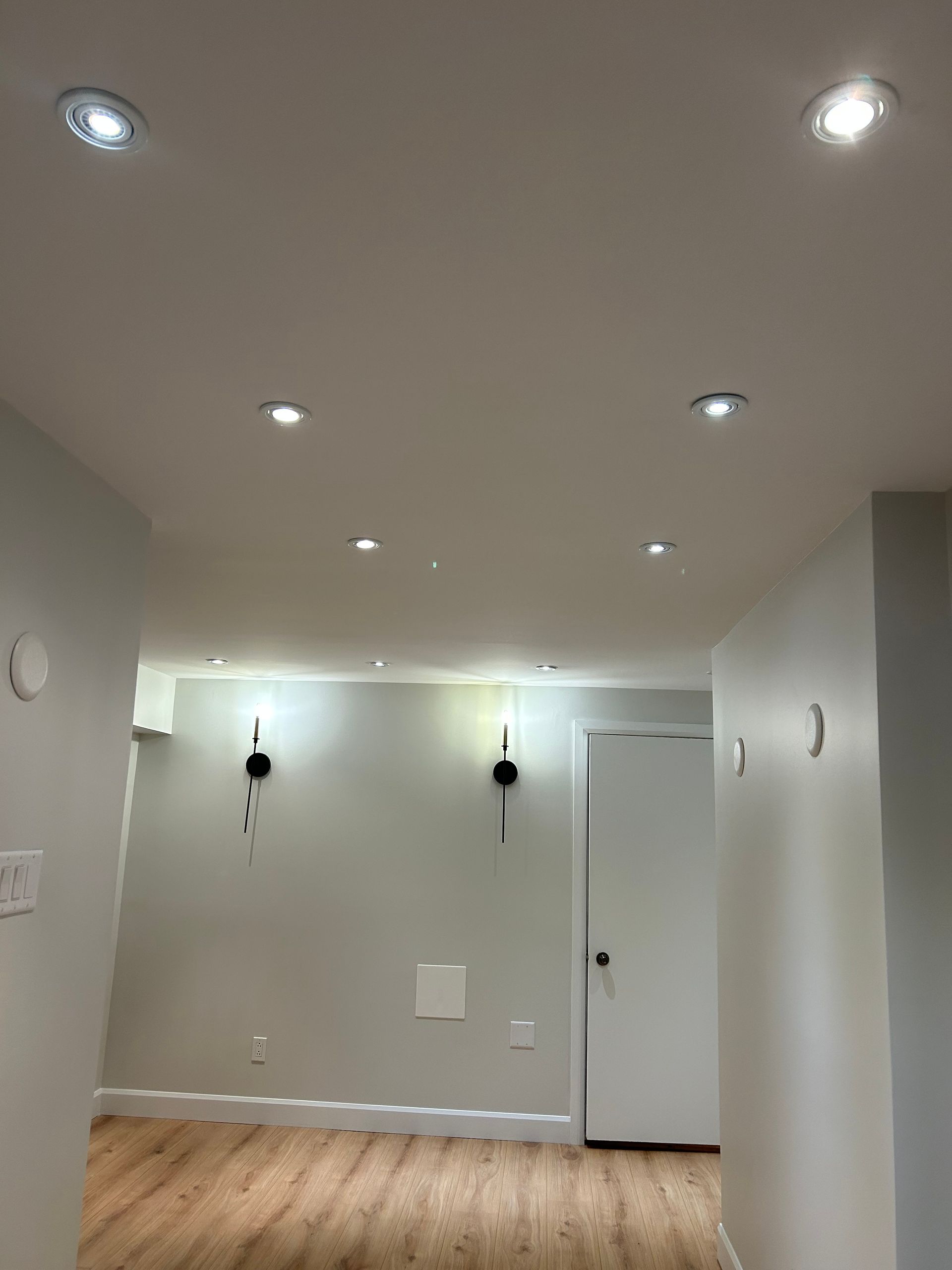 Couloir avec spots encastrés au plafond, murs blancs, plancher en bois et porte fermée.