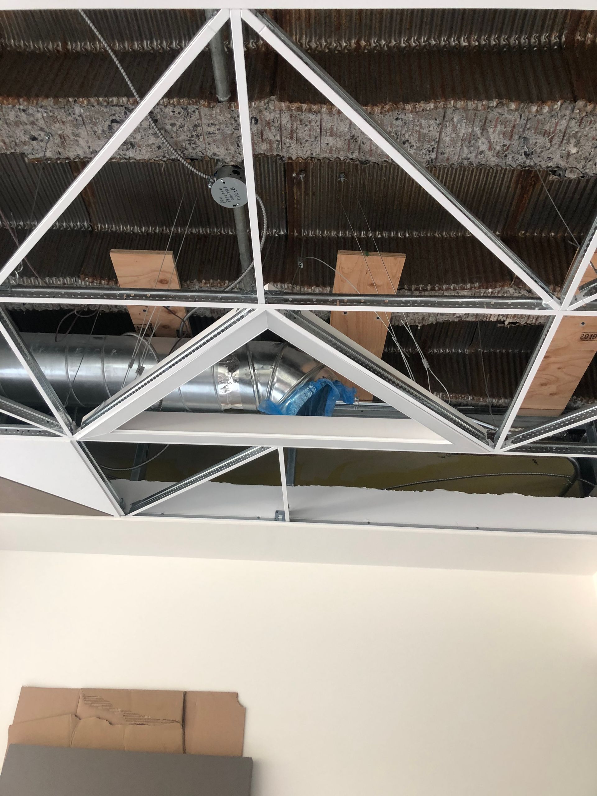 Plafond géométrique blanc avec conduits et supports structurels apparents.