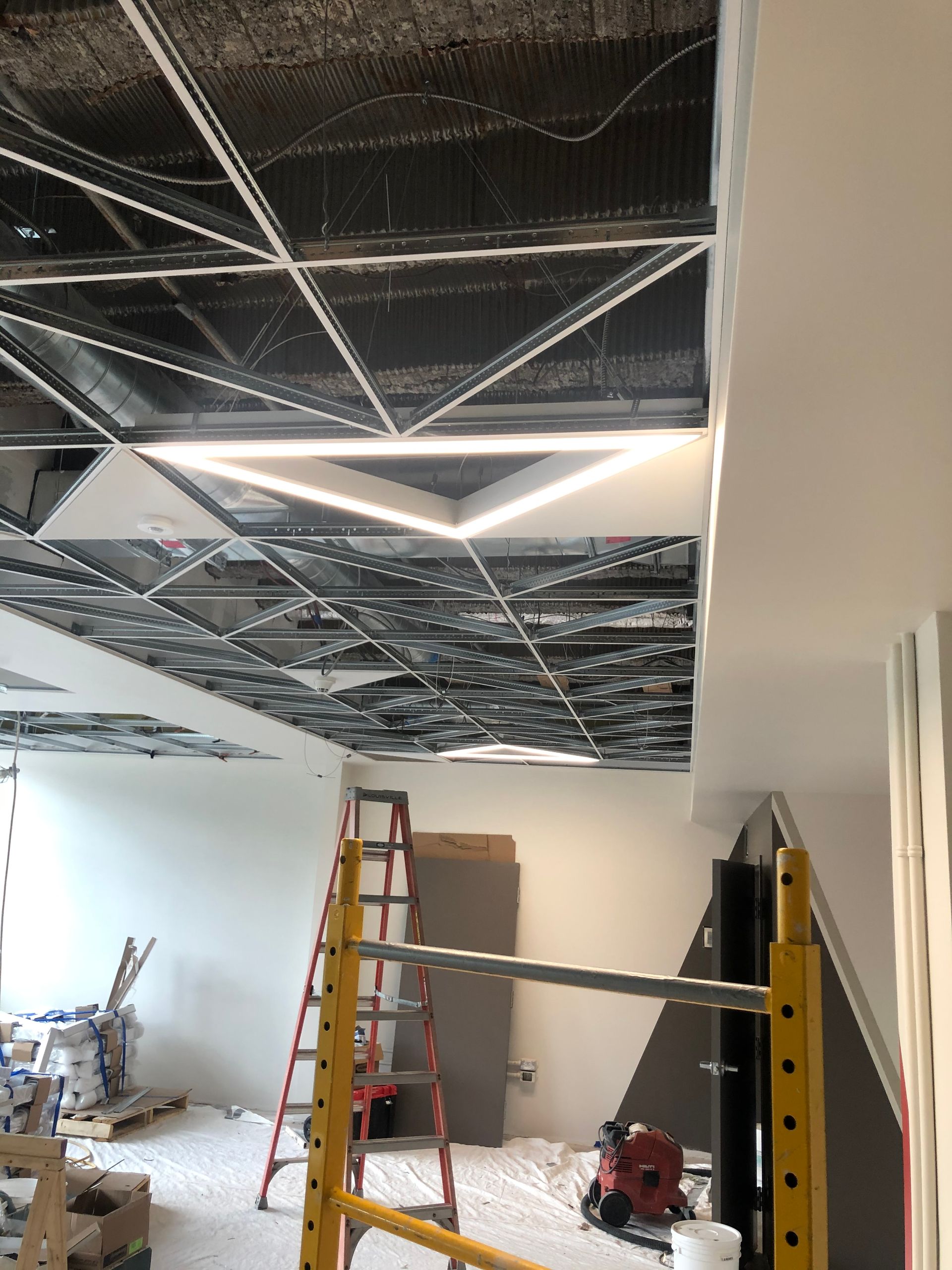 Chantier : Conception de plafond géométrique avec éclairage installé ; échelle et échafaudage.