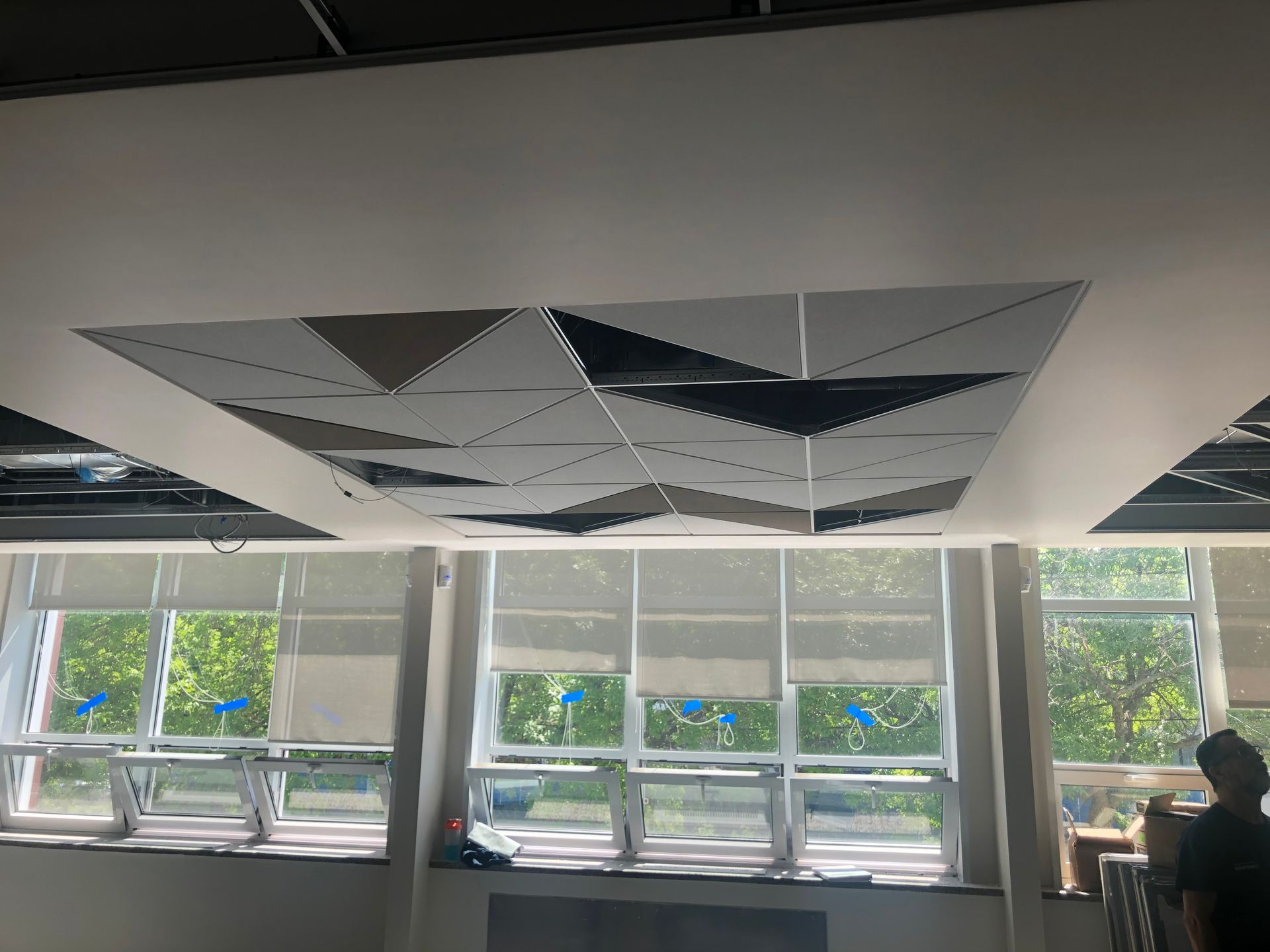 Dalles de plafond géométriques au-dessus des fenêtres dans une pièce lumineuse ; une personne dans l'ombre.