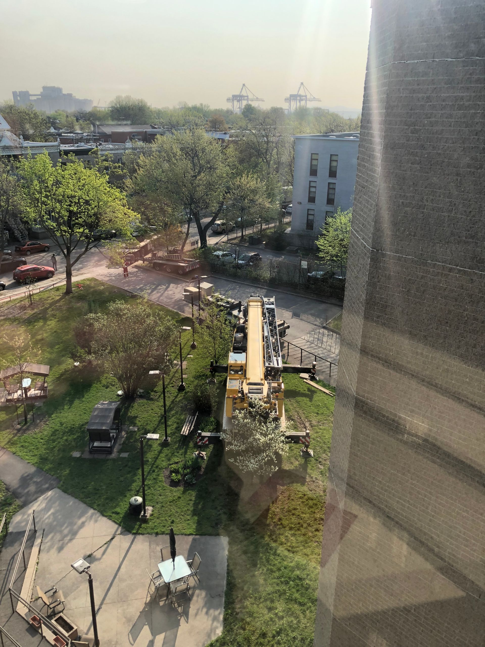 Surplombant un parc avec des arbres, des sentiers et une structure en bois ; toile de fond de paysage urbain, ciel brumeux.