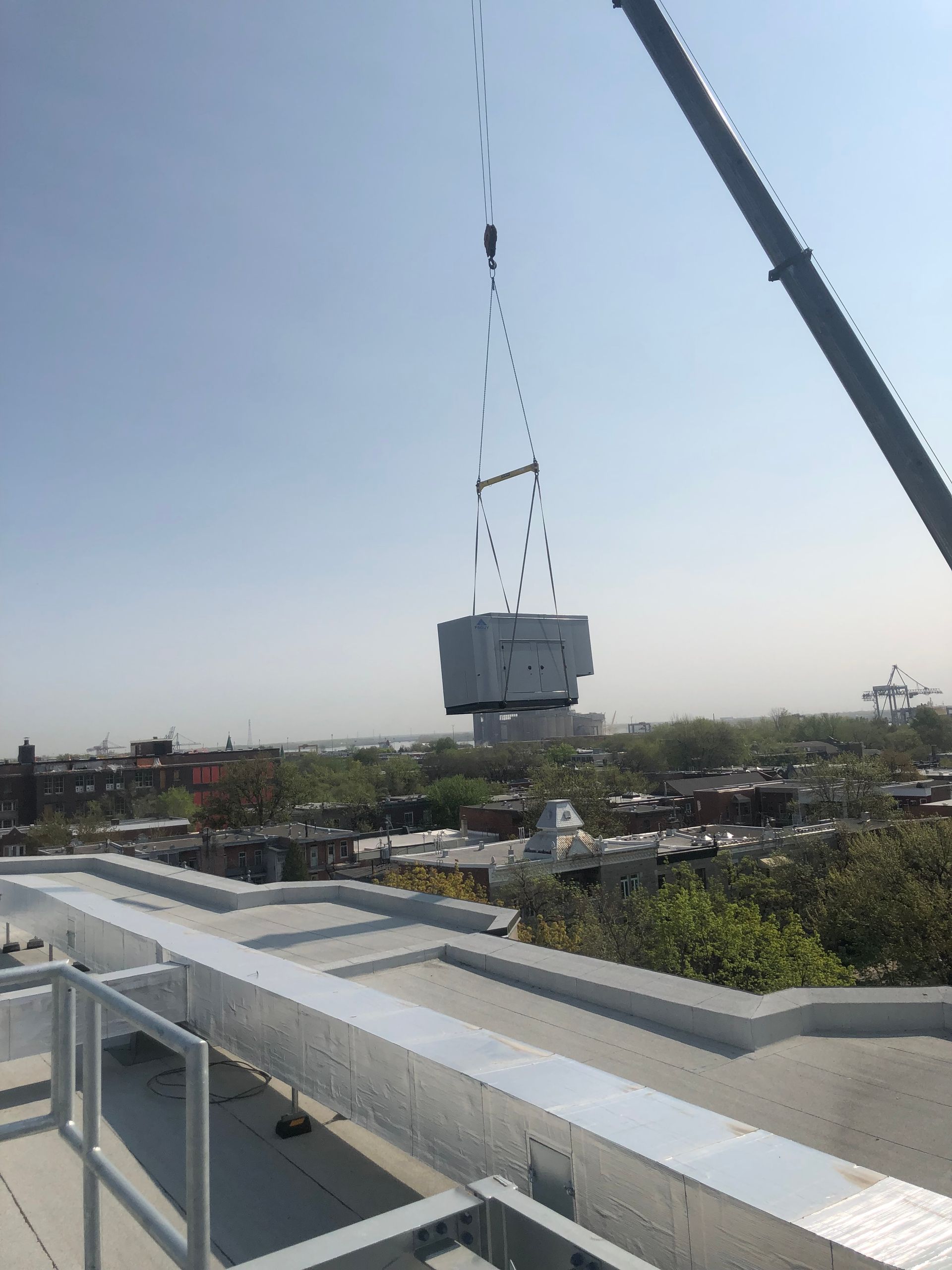 Une grue soulevant un grand transformateur électrique au-dessus d'un paysage urbain.