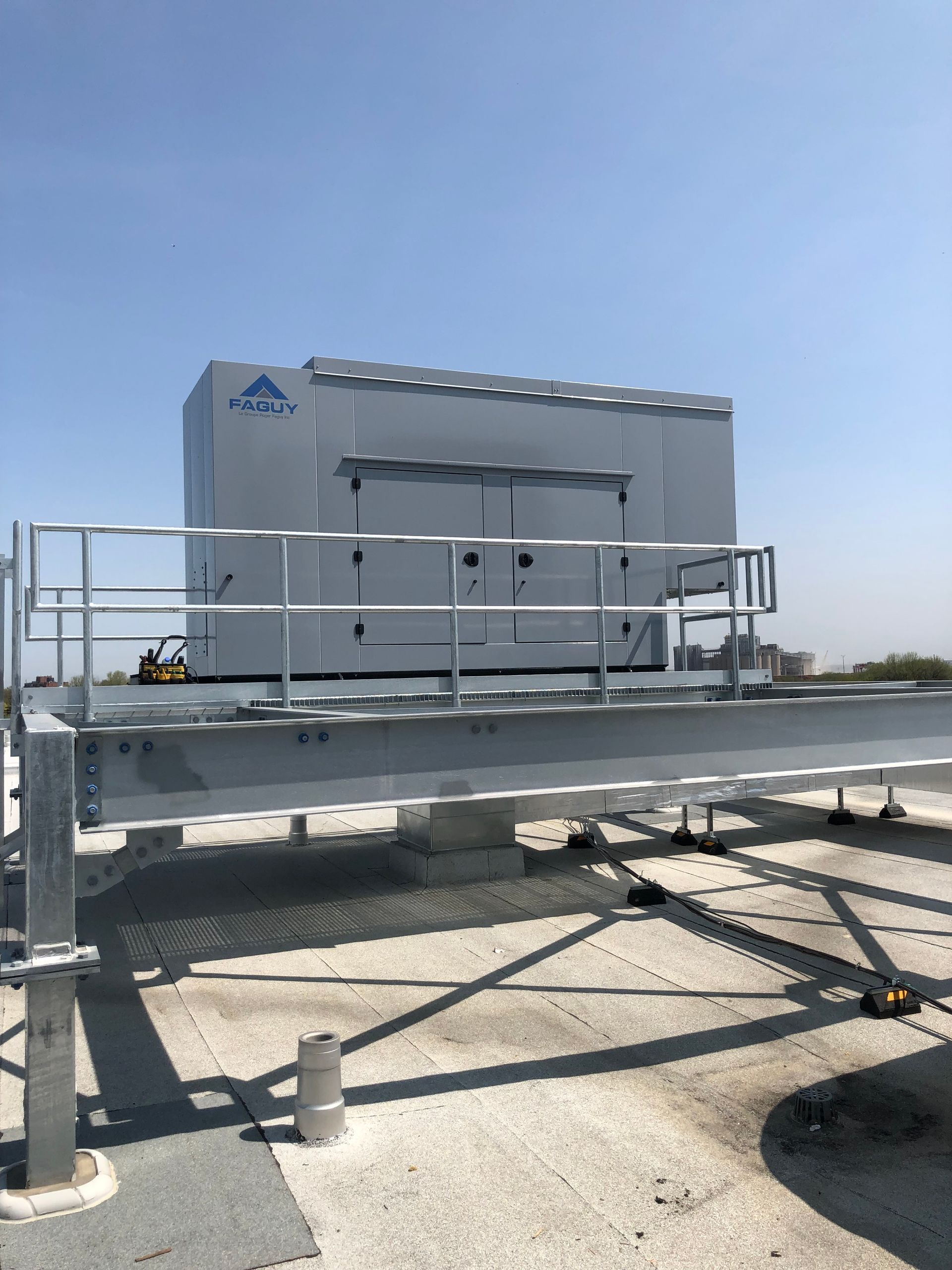 Grande unité industrielle blanche au sommet d'une plate-forme avec garde-corps, sur un toit, sous un ciel bleu.