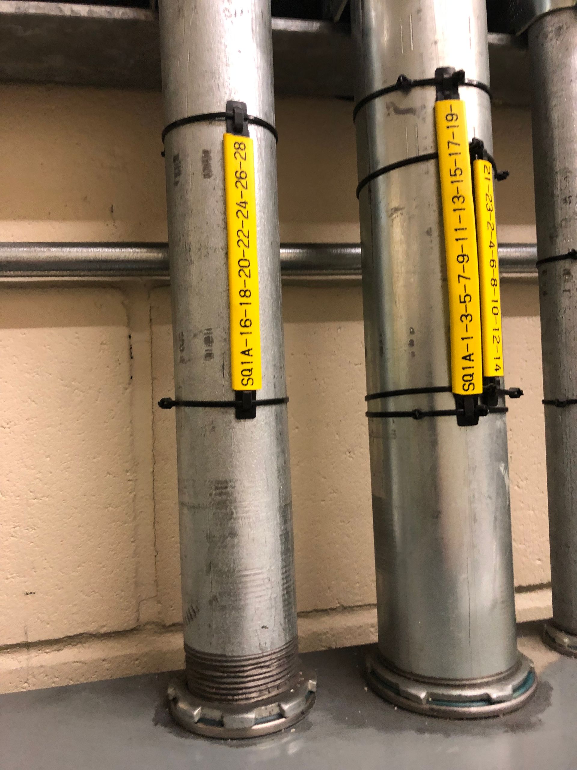 Des tuyaux métalliques avec des étiquettes jaunes, fixés avec des attaches zippées noires, sont fixés au sol.